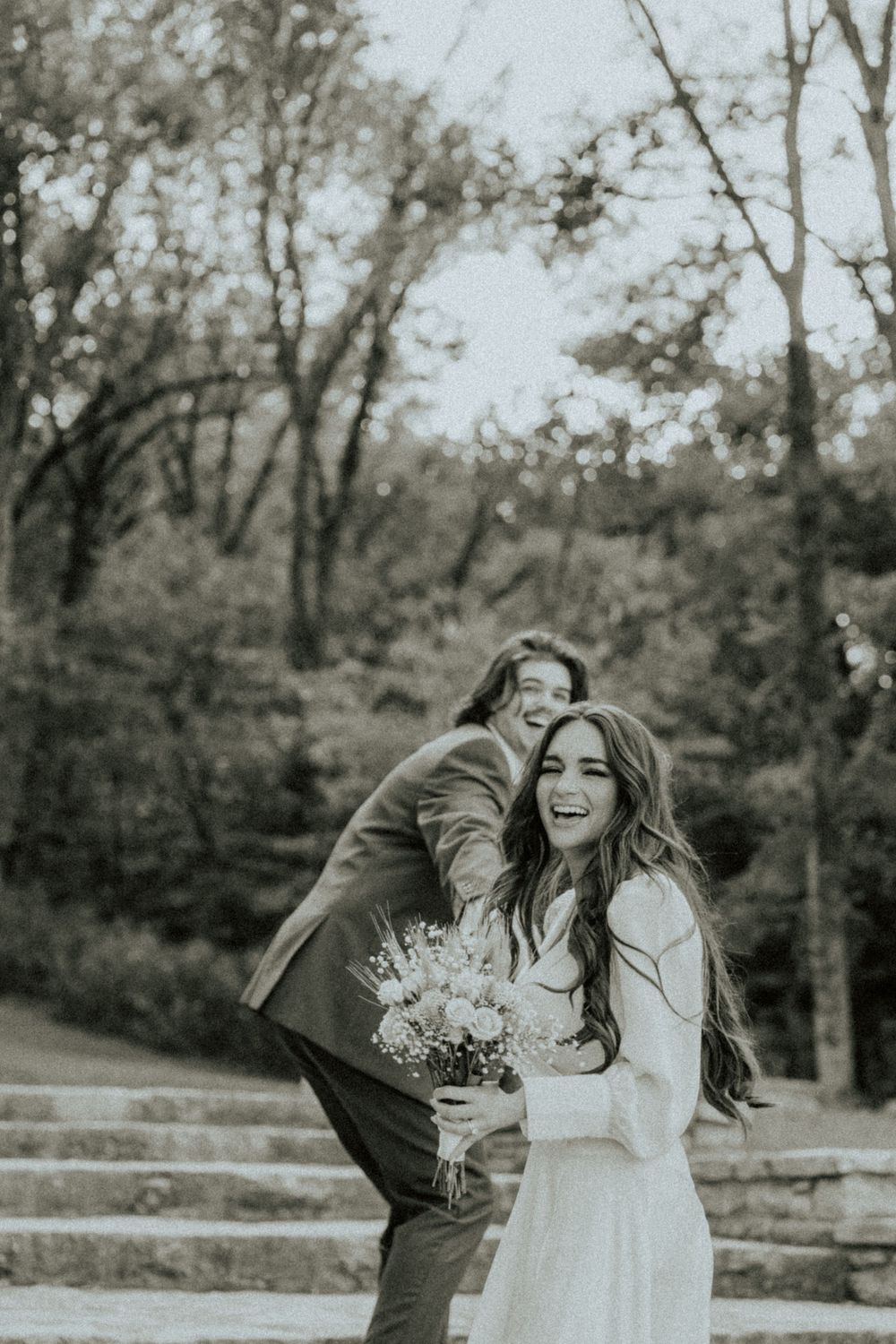 A playful wedding moment captured in black and white with natural wooded background.