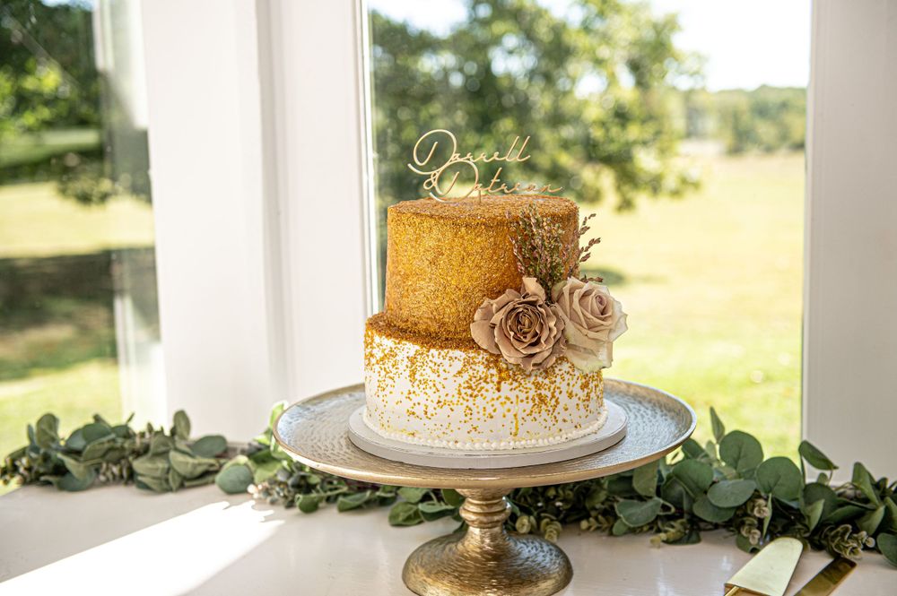 Elegant gold and white wedding cake decorated with roses on an antique metal stand.