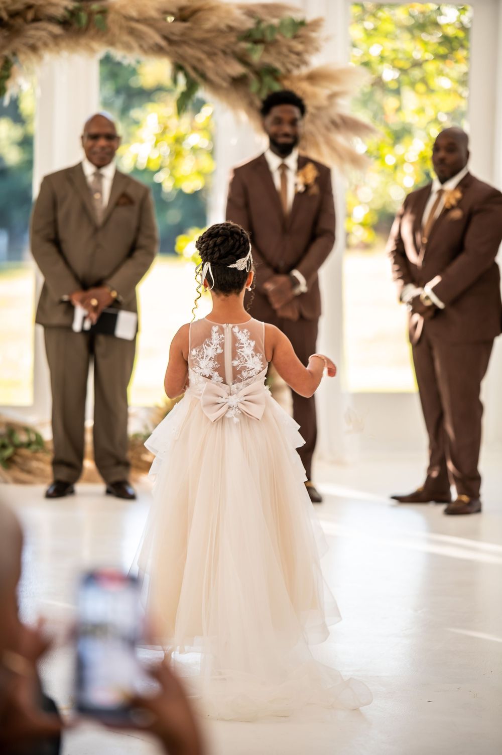 A wedding ceremony view from behind showing a tulle dress and brown suited attendants.