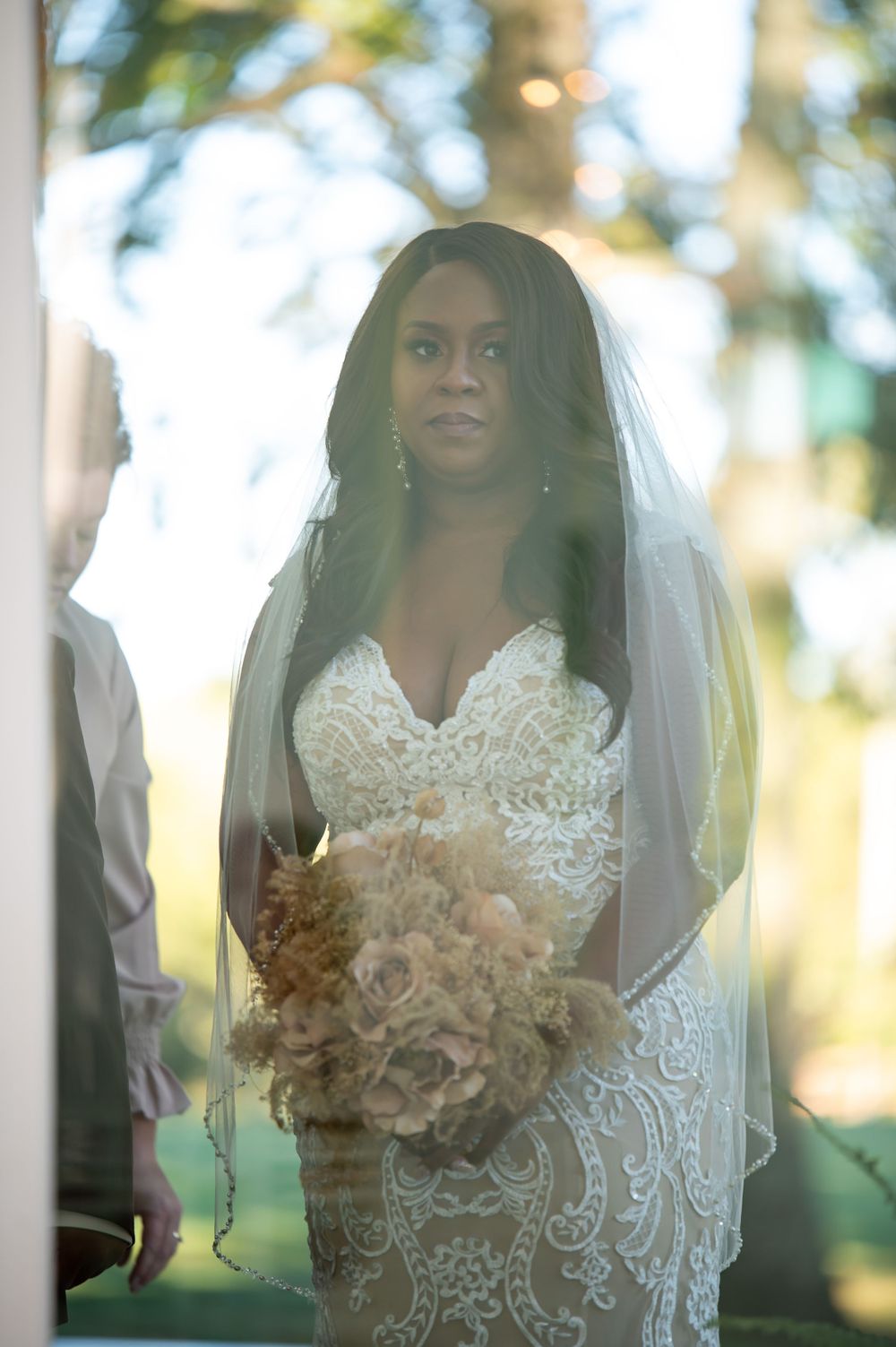 A bridal portrait showcasing an intricate lace gown and flowing veil in natural light.