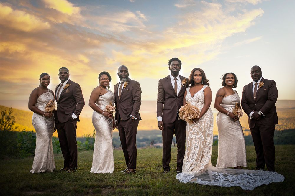 Wedding party poses against a sunset mountain backdrop in elegant attire.