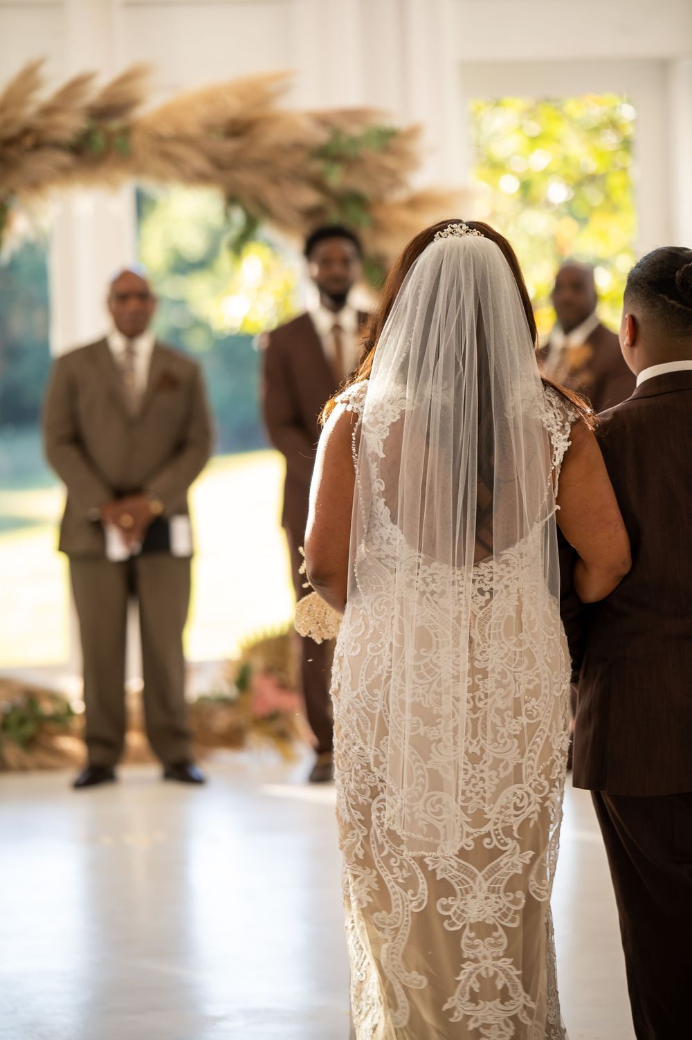 Back view of a bride in a lace dress with veil during an indoor wedding ceremony.