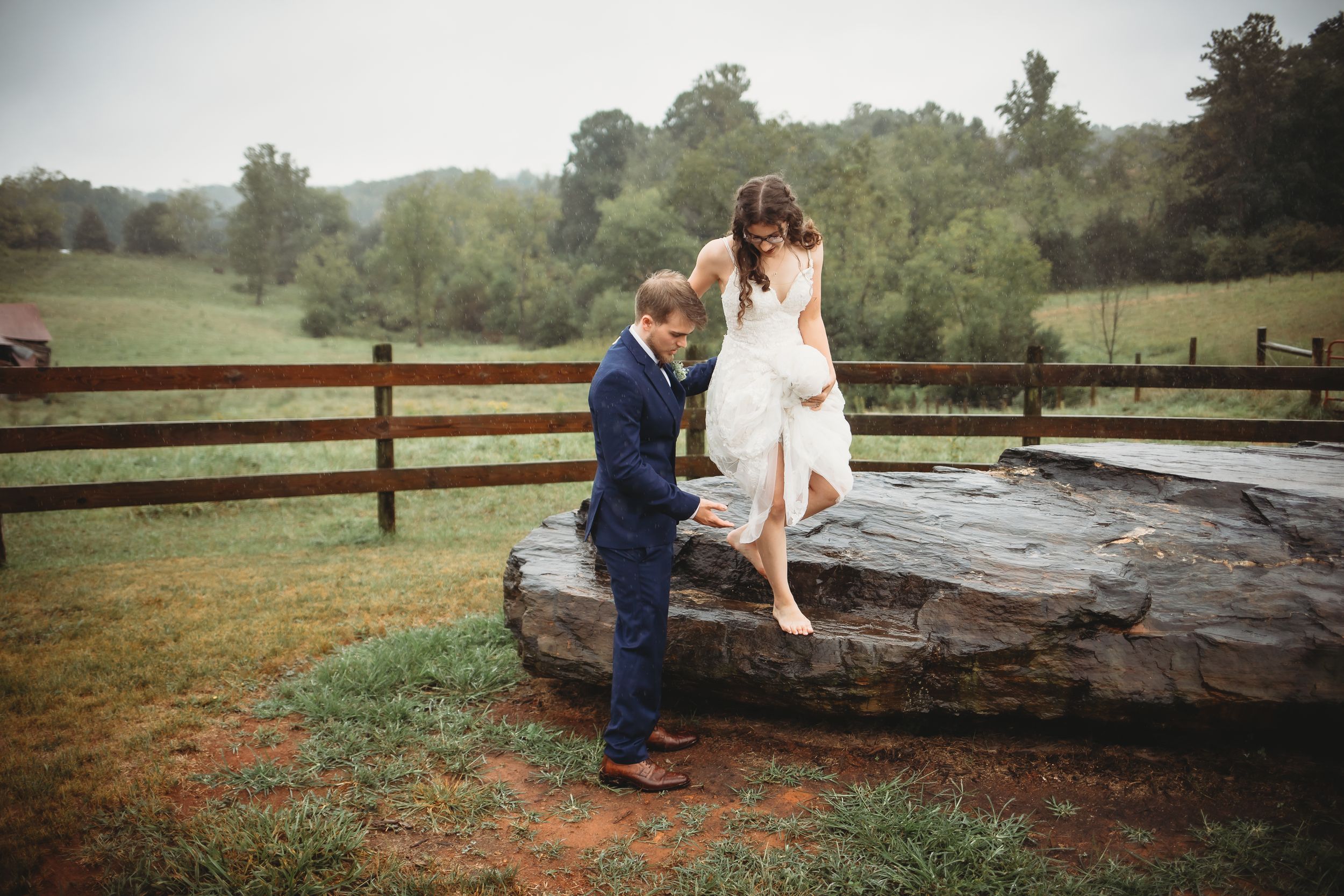 A romantic moment captured on a large rock with rustic wooden fencing in the background.