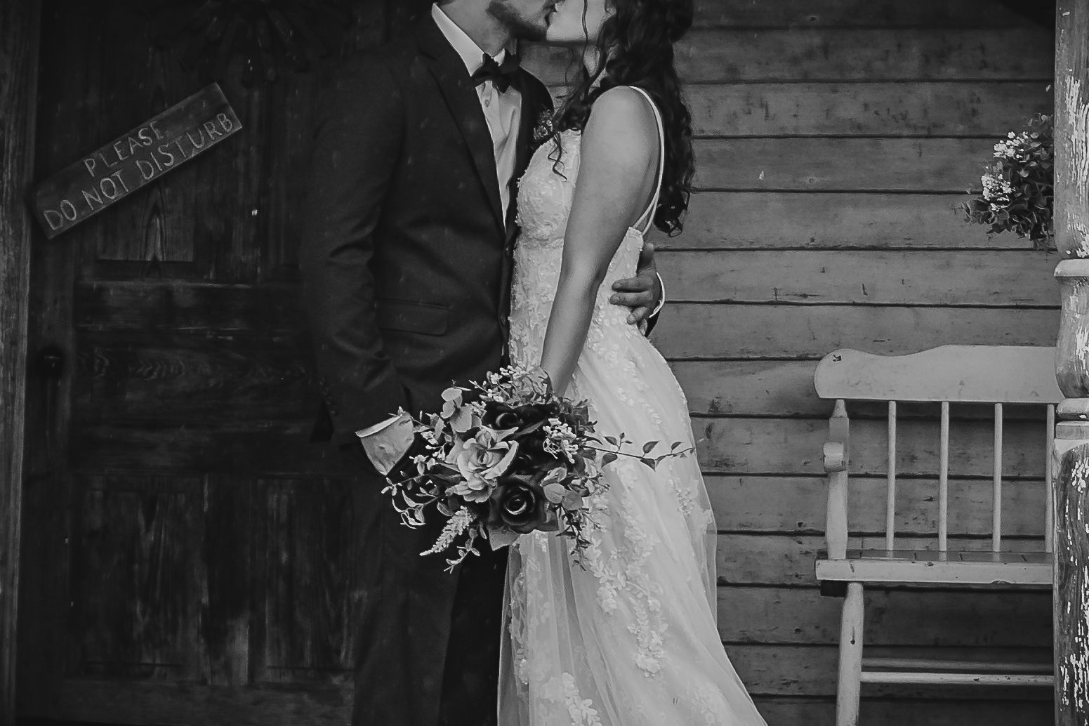 Moody black and white wedding portrait with rustic wooden backdrop and floral bouquet.