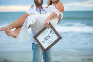 Romantic beach photo with couple holding 'The End' sign against ocean waves.