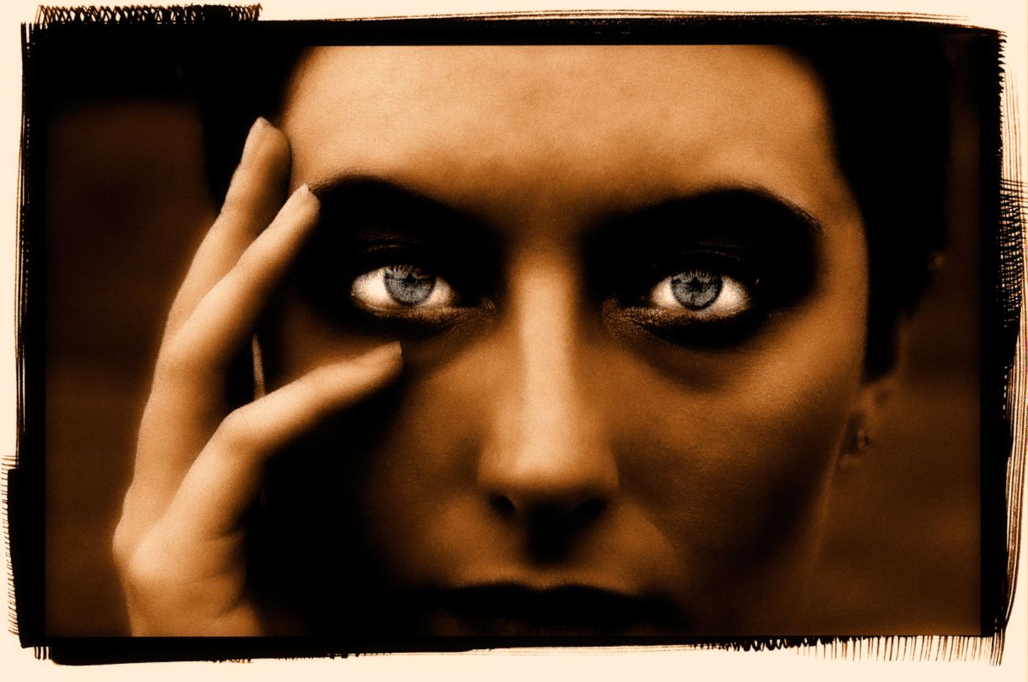 Dramatic sepia portrait with intense eyes and hand gesture against dark background.