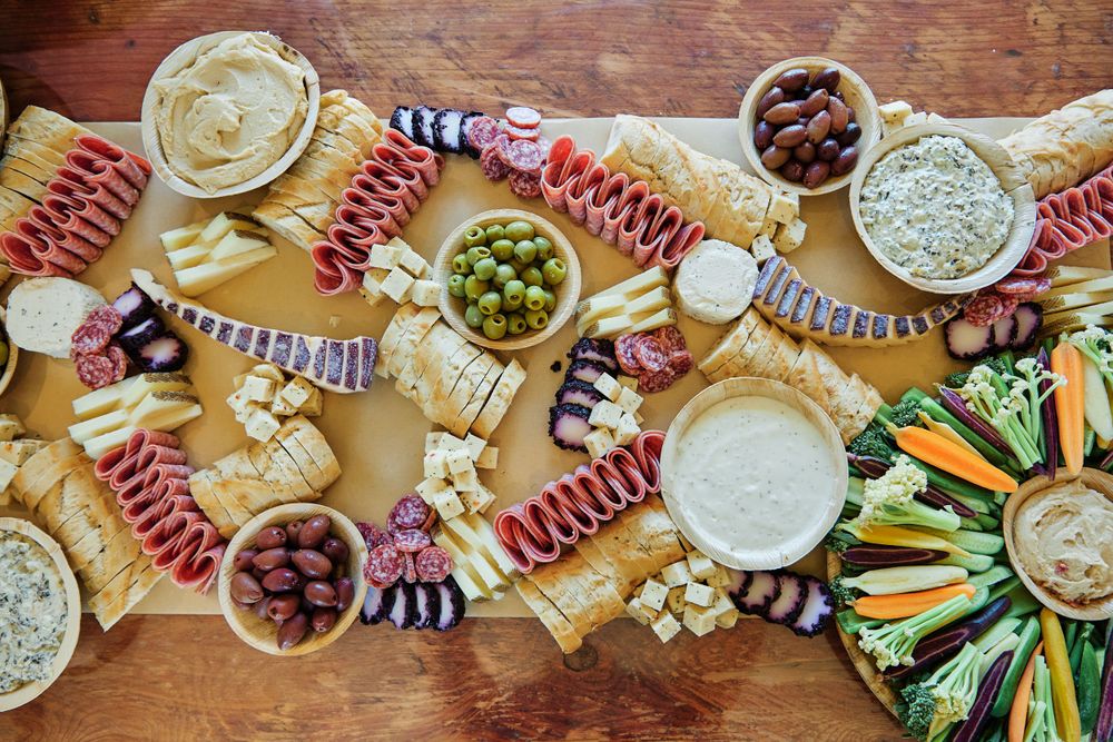 Overhead view of a wooden table spread with appetizers, dips, and charcuterie items.