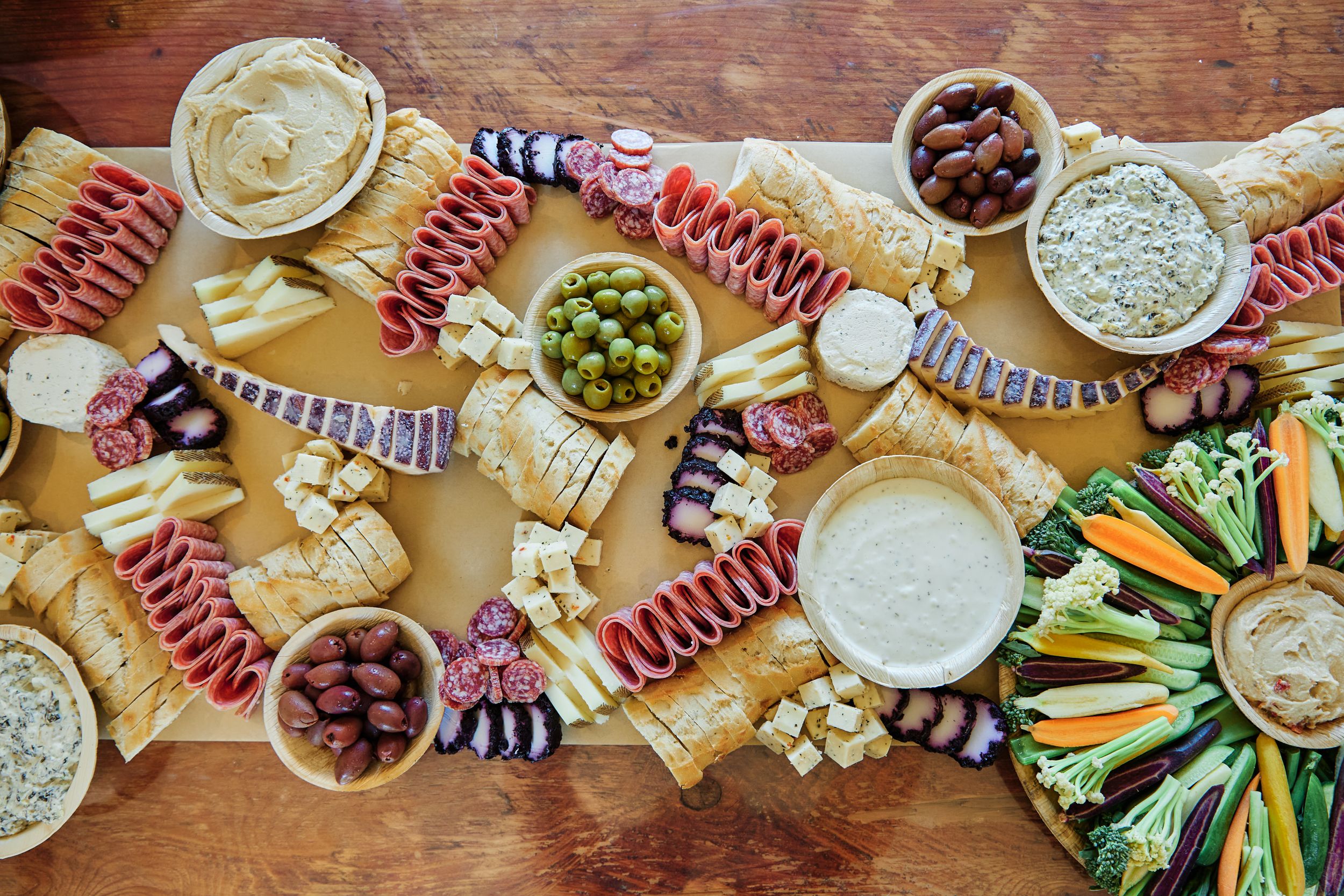 Overhead view of a wooden table spread with appetizers, dips, and charcuterie items.