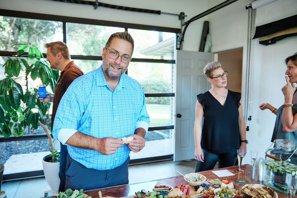 Casual gathering around a table with food and drinks in a bright indoor space.