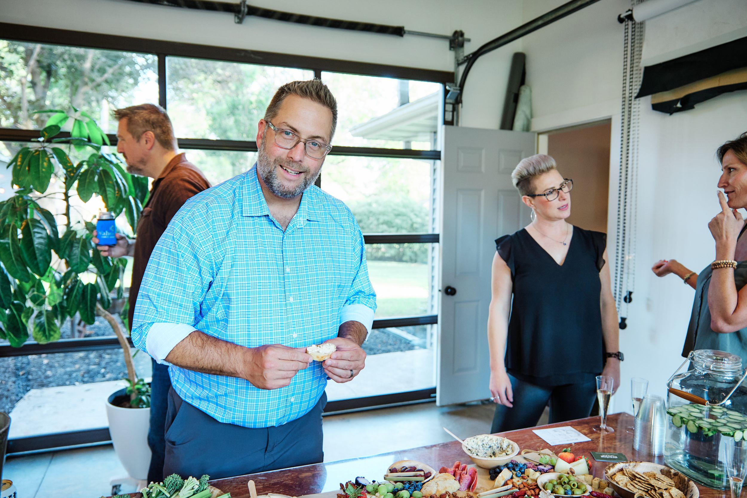 Casual gathering around a table with food and drinks in a bright indoor space.