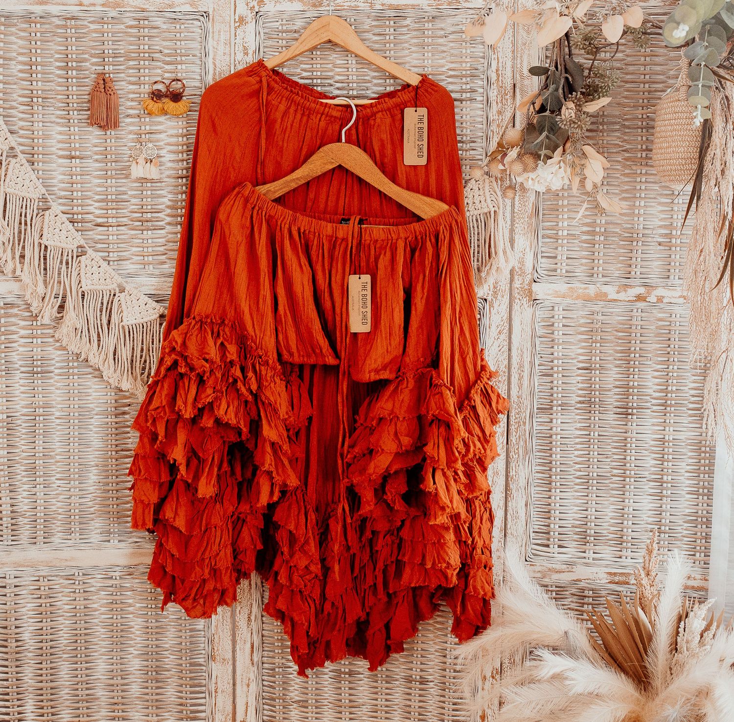 Orange and red ruffle dresses displayed on hangers against a white wicker background.