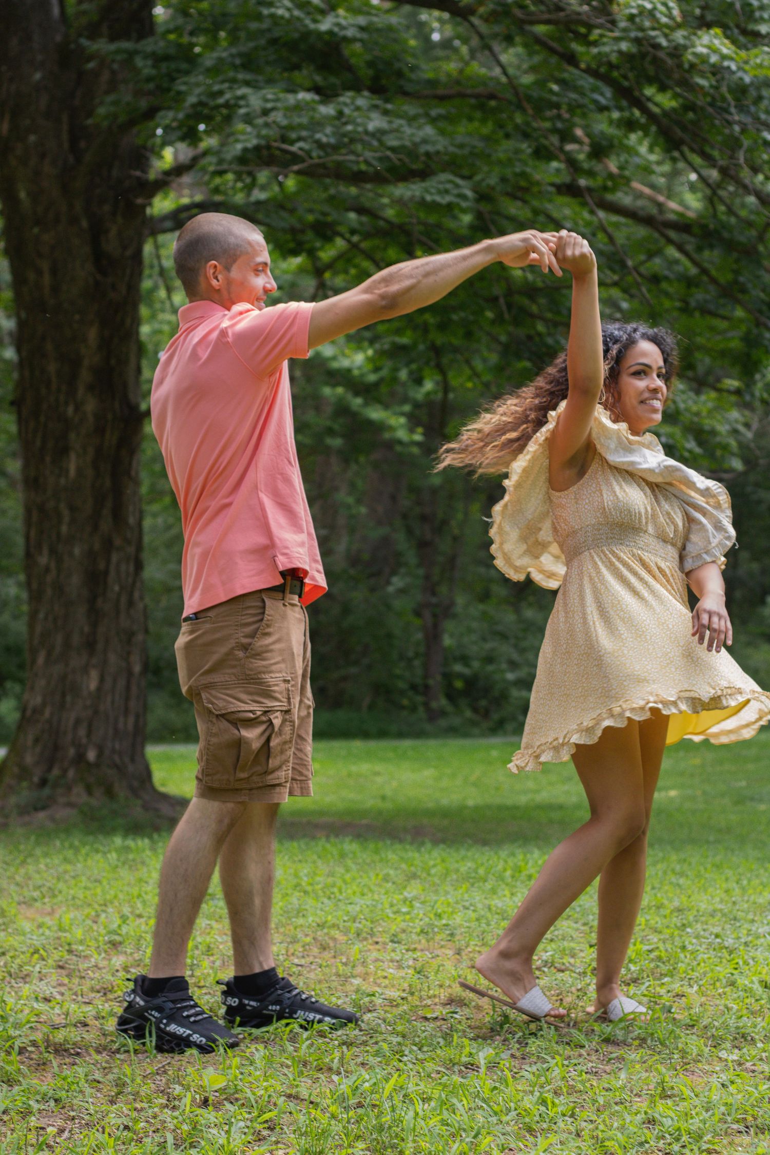 Playful couple dancing together on grass in a park during a summer day.