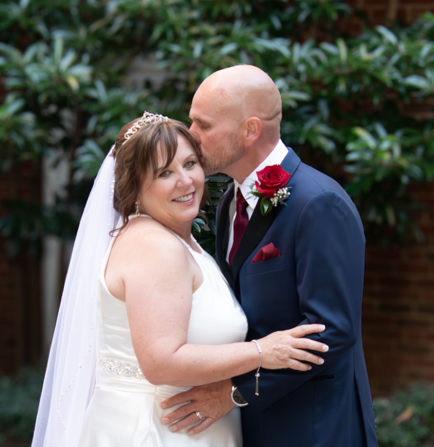 Couple in wedding attire sharing an intimate moment in front of greenery.