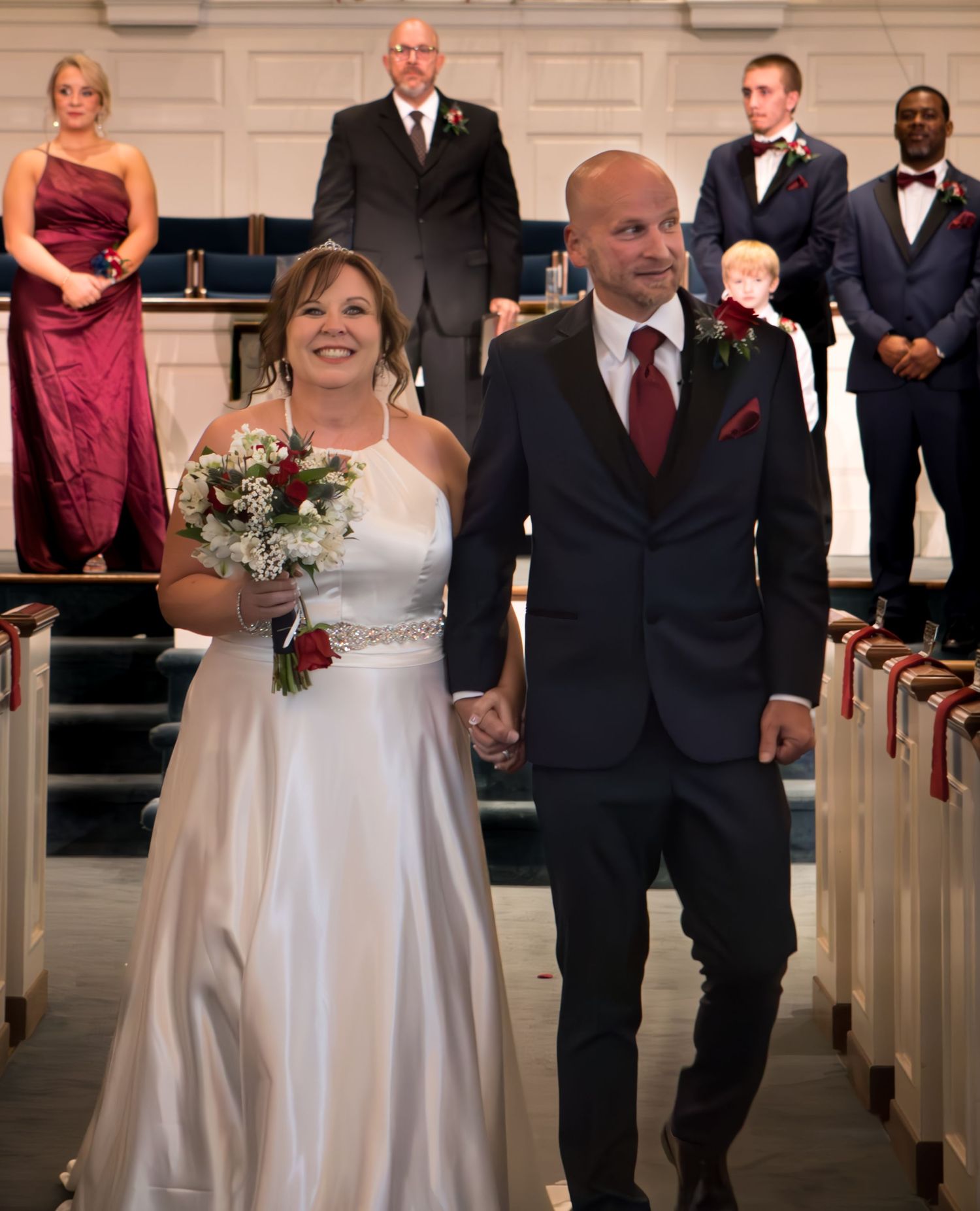 Wedding party members walking down the church aisle in formal attire.