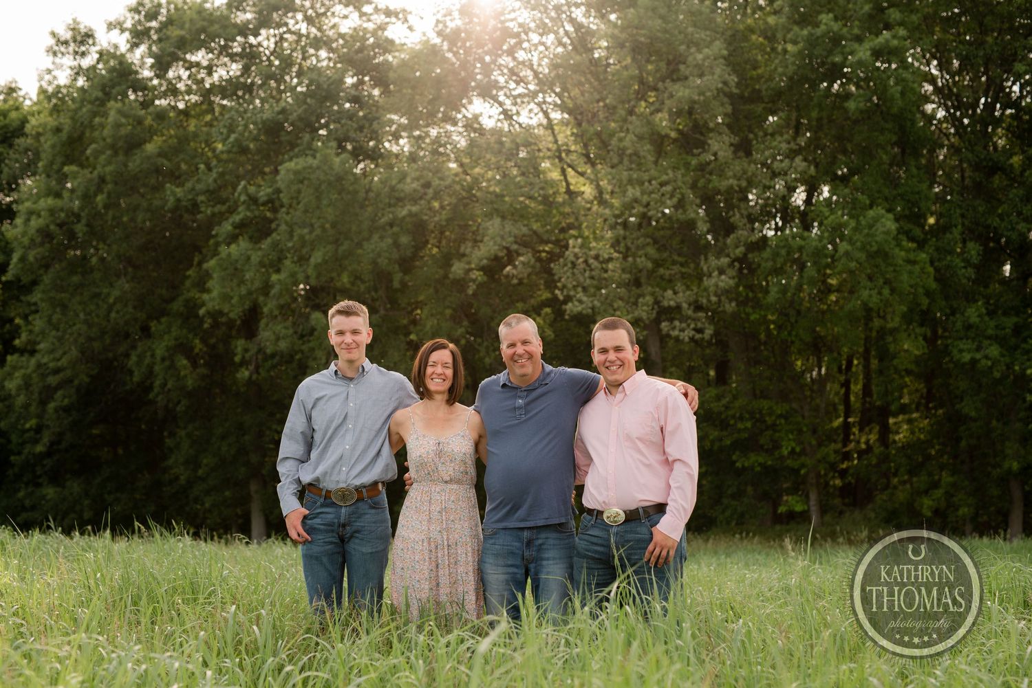 Family photo of group standing together in a green field at golden hour.