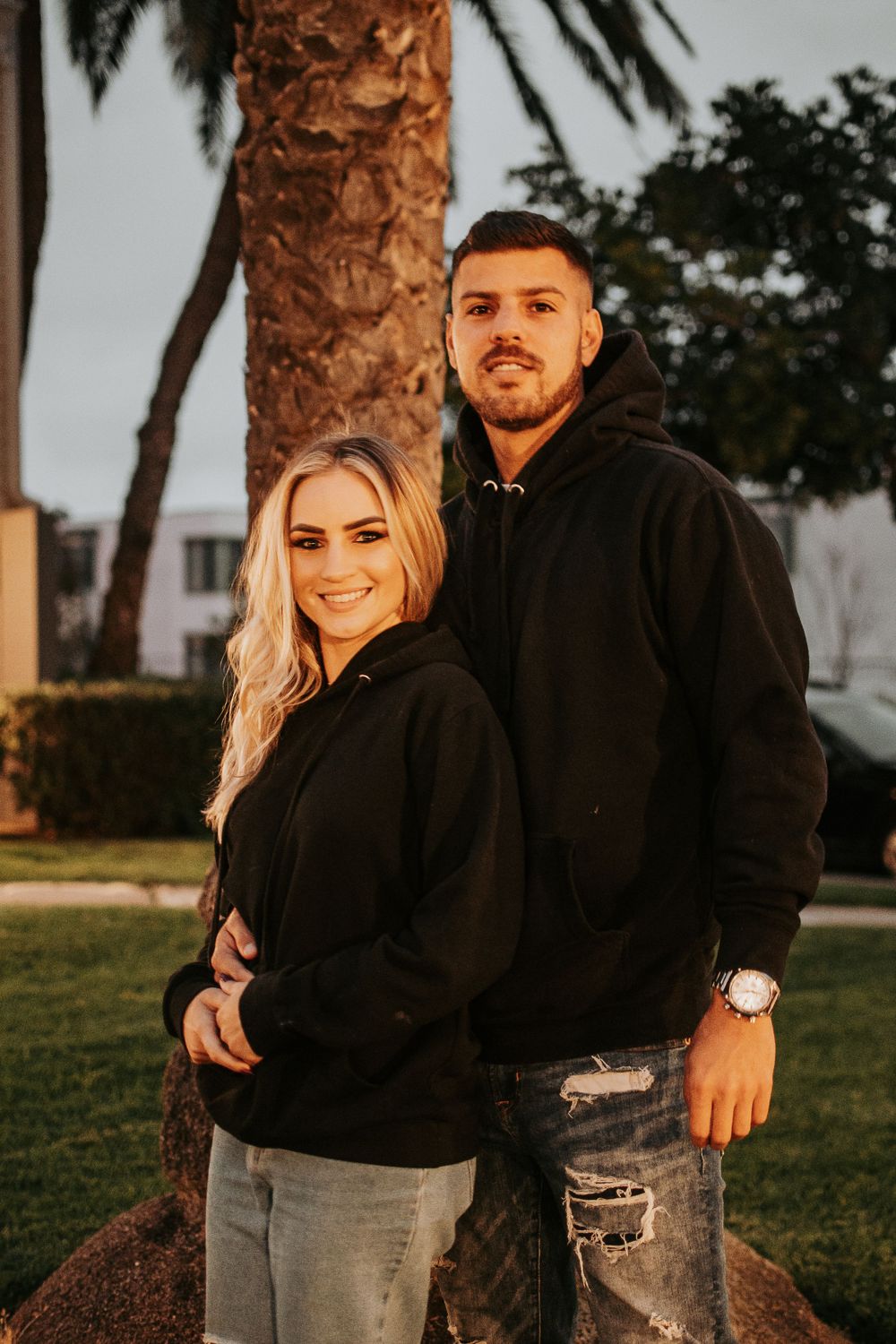 Sunset portrait against palm trees wearing black hoodies and ripped jeans.