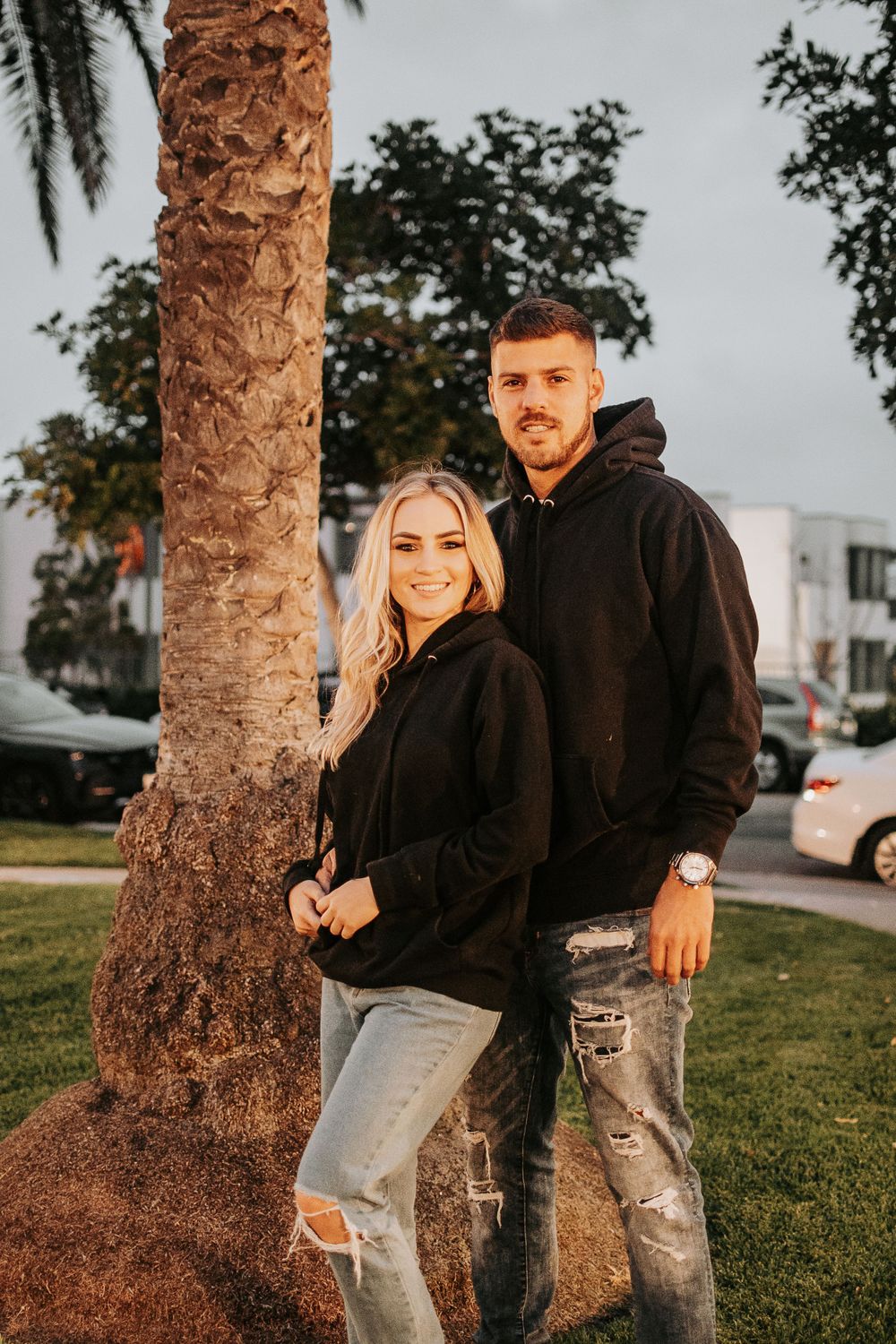 Golden hour portrait by palm tree trunk in casual black and denim outfits.