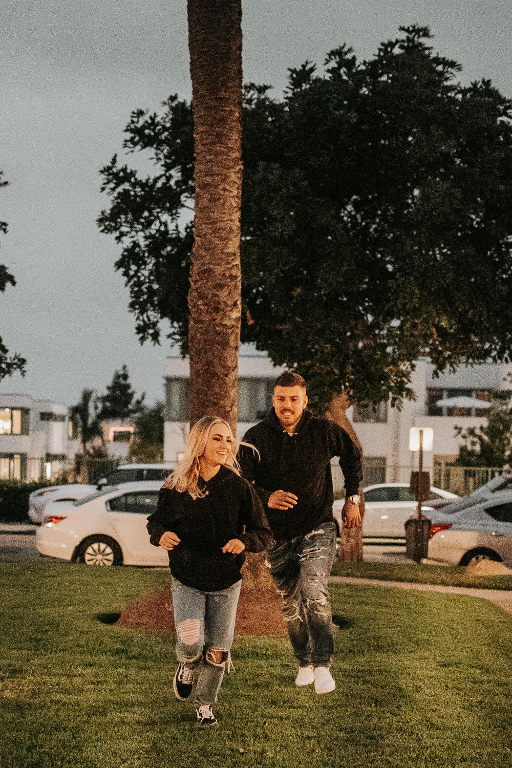 Two people run and play together on a grassy hill during golden hour.