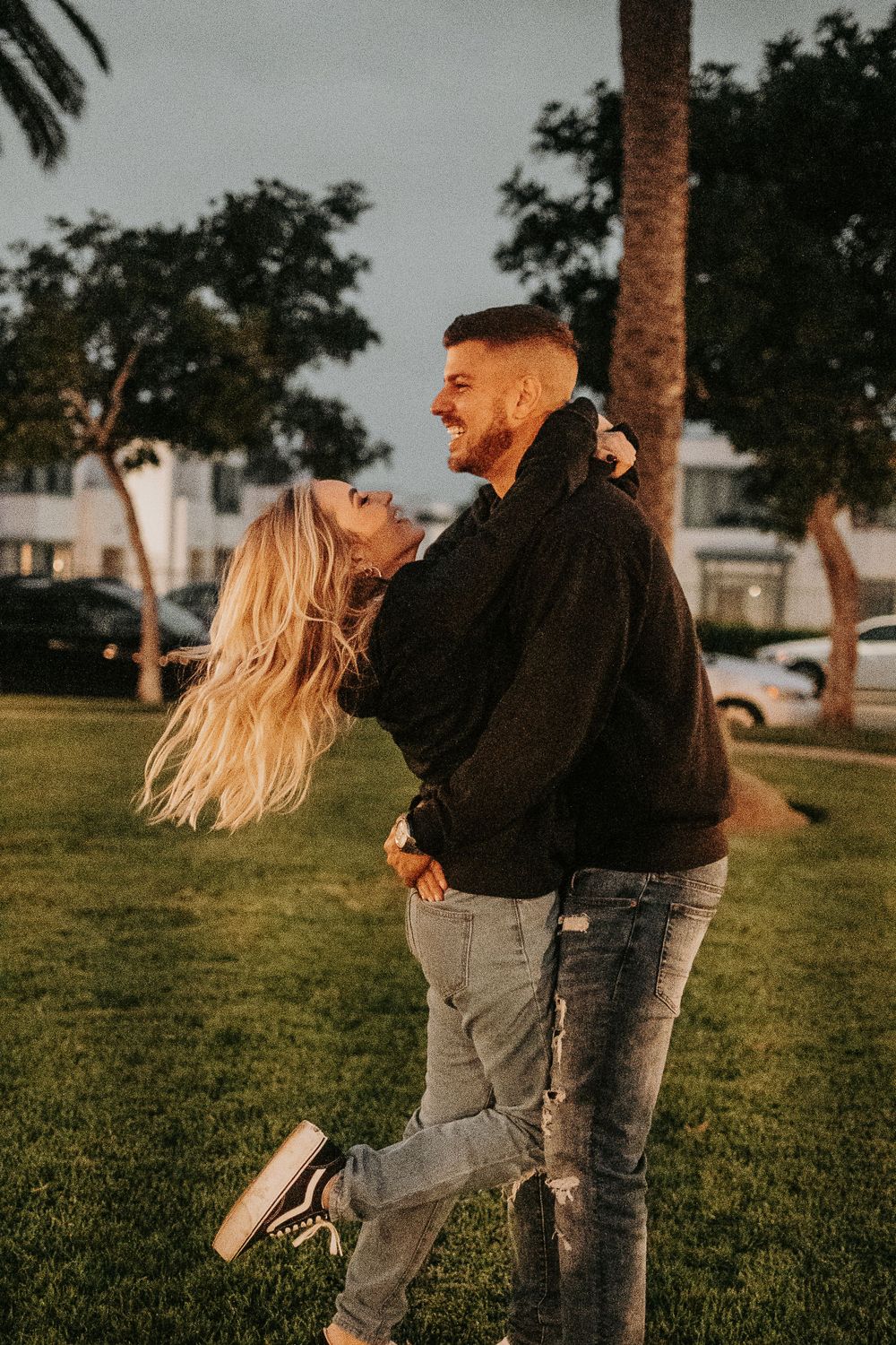 Two people embrace and laugh while playing on grass during sunset.