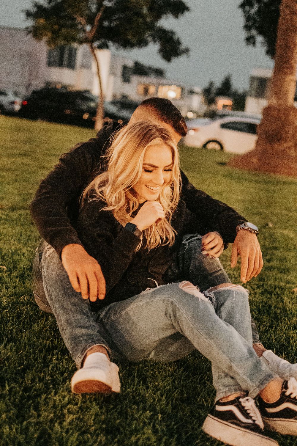 Two people share a tender moment while relaxing on grass at sunset.