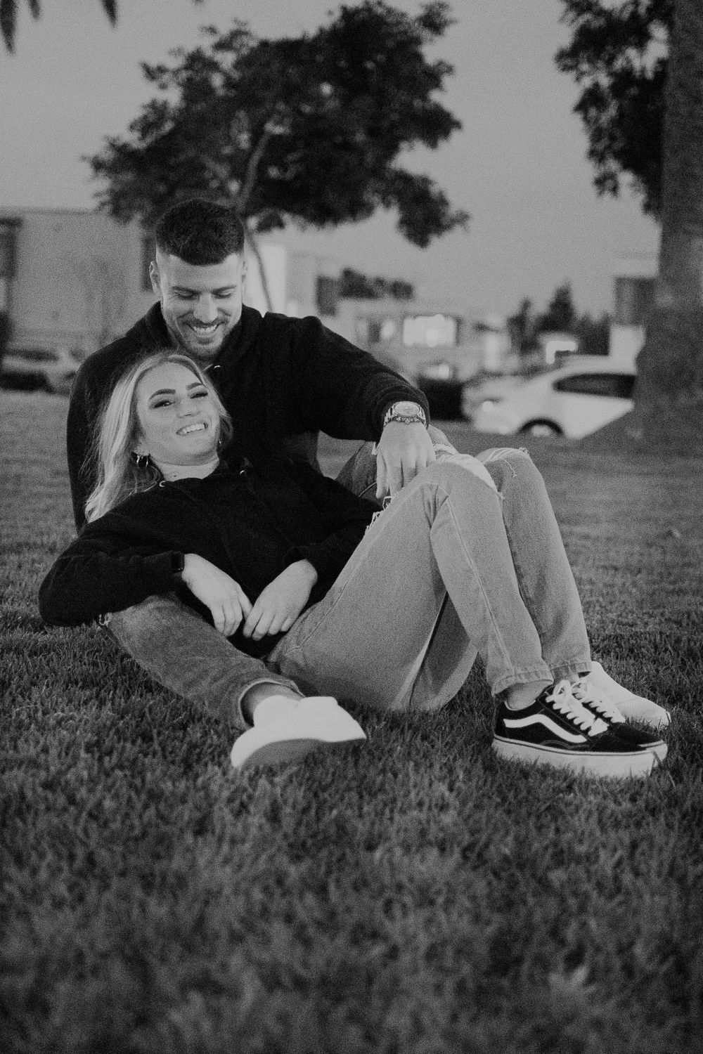 A couple lays together on grass during a playful photoshoot.