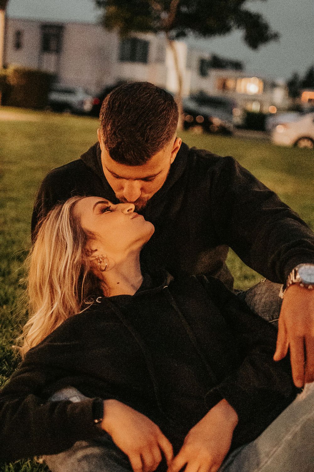 Romantic couple in black attire sharing intimate moment during golden hour sunset.