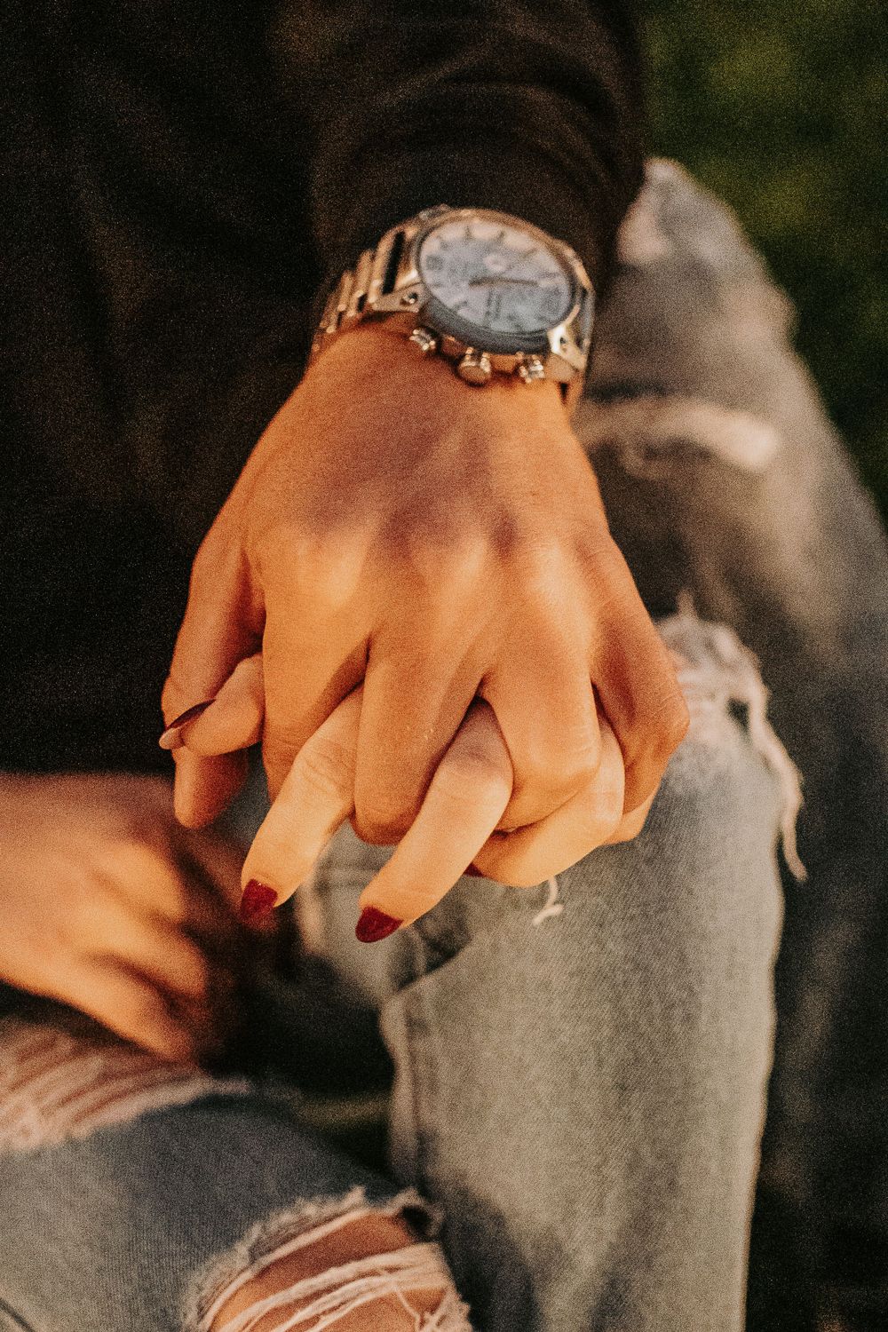 Hand wearing watch resting on ripped jeans in warm sunlight.