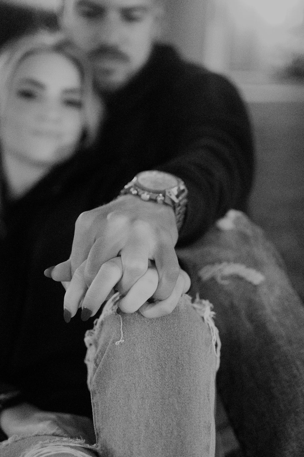 Black and white close-up of hands resting on distressed denim jeans.