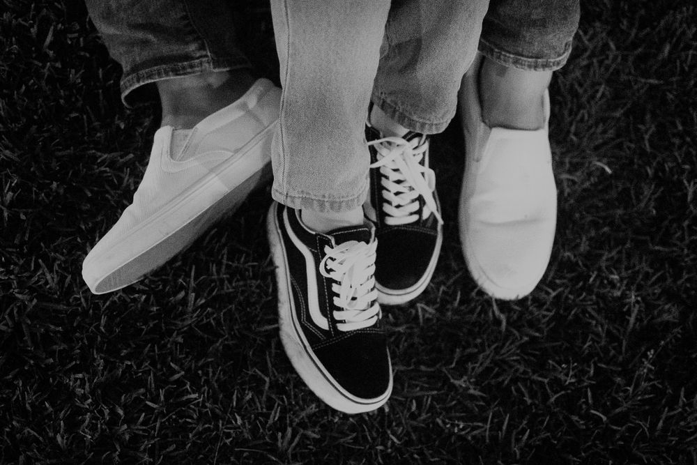Black and white photo of sneakers and legs sitting on grass.