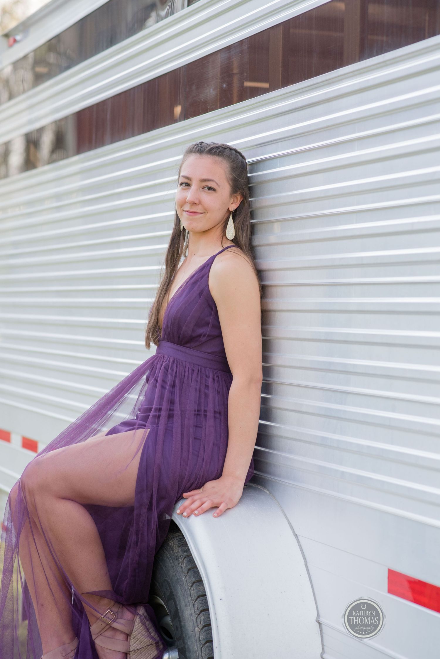 Someone poses in a flowing purple dress against a white trailer exterior.