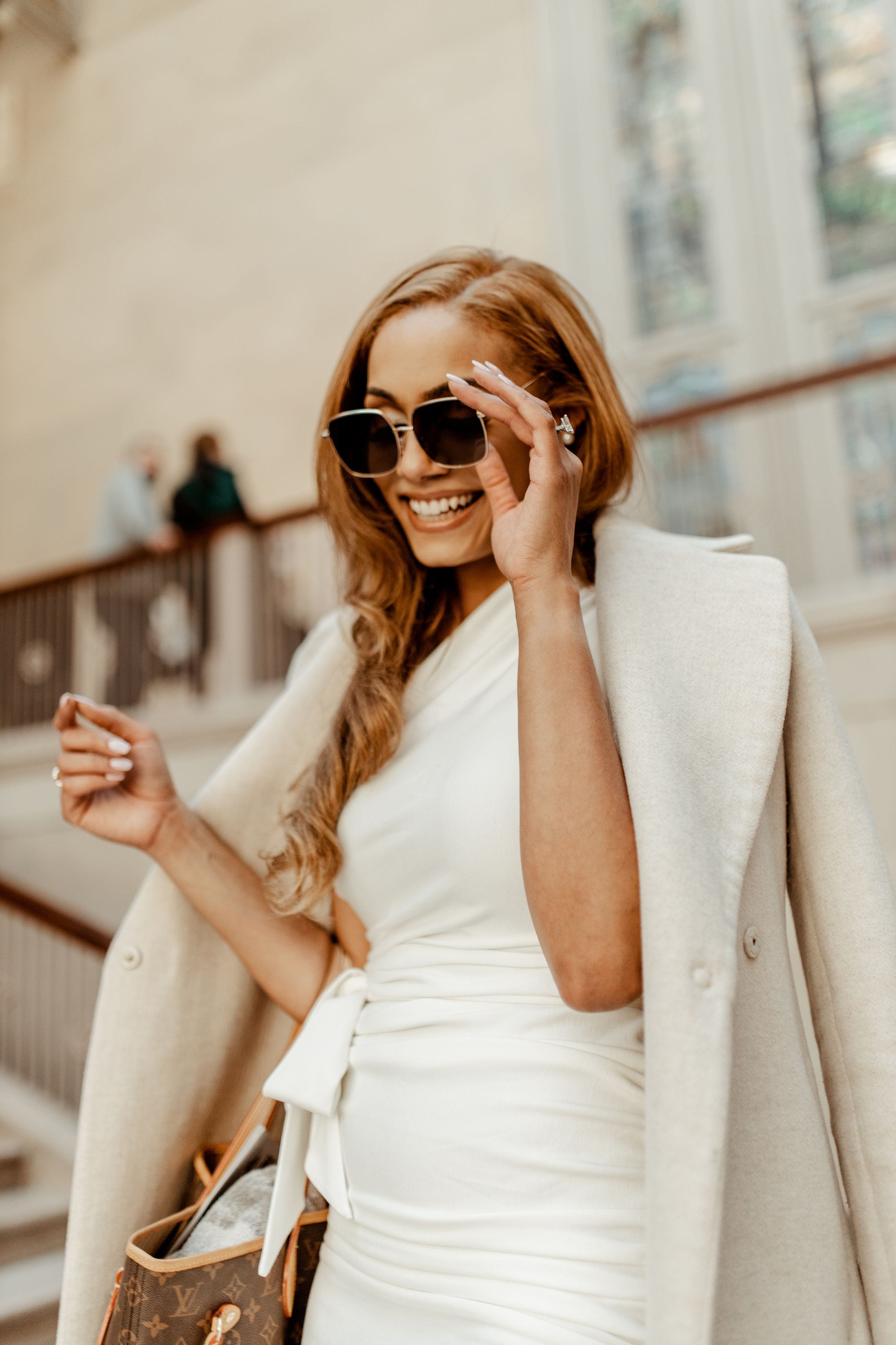 Stylish woman in white dress and sunglasses posing joyfully on stone staircase.