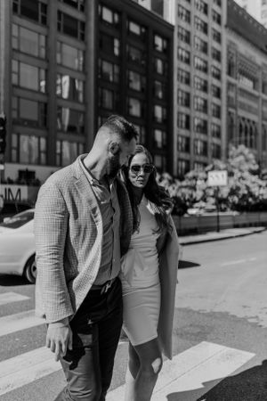 Urban couple in business casual attire walking together on city street in black and white.