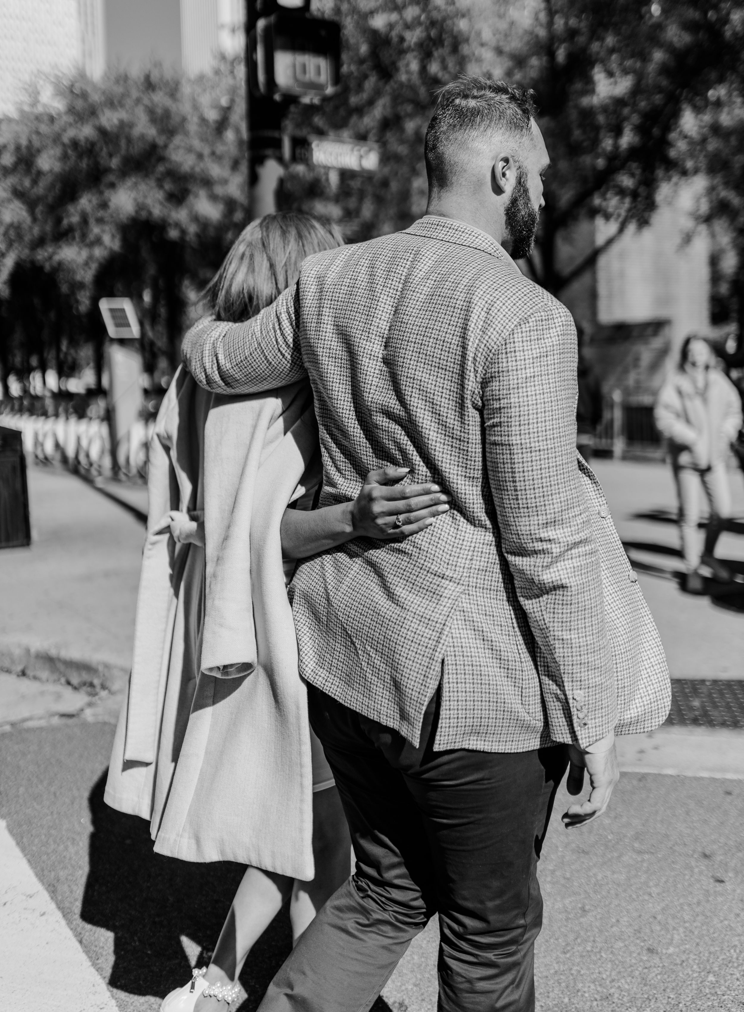 Black and white photo of couple walking arm in arm down city sidewalk.