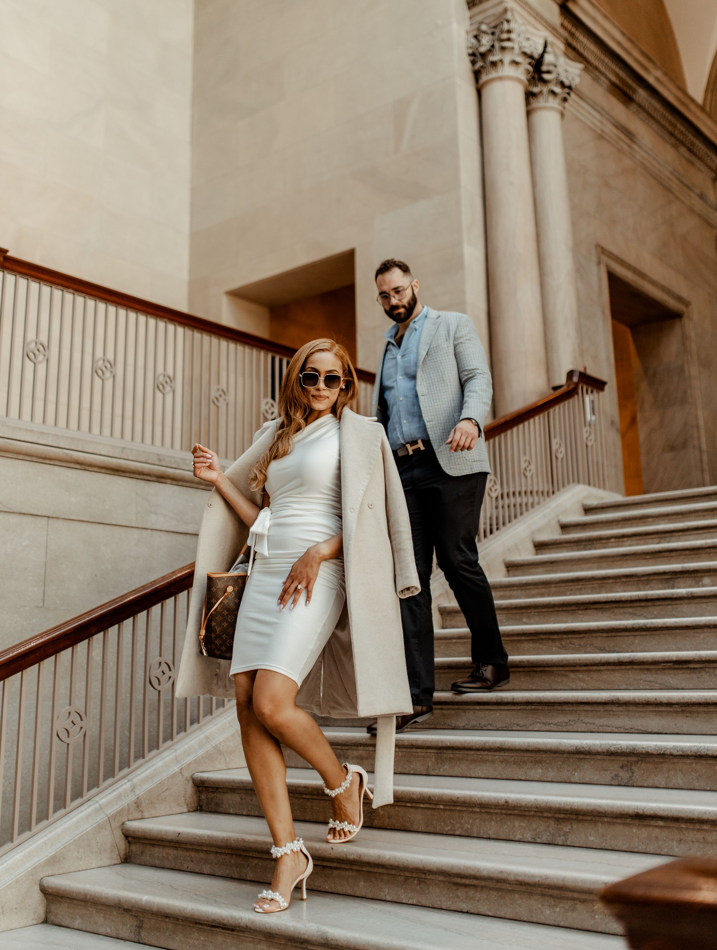 Fashionable couple posing on elegant stone staircase in urban setting.