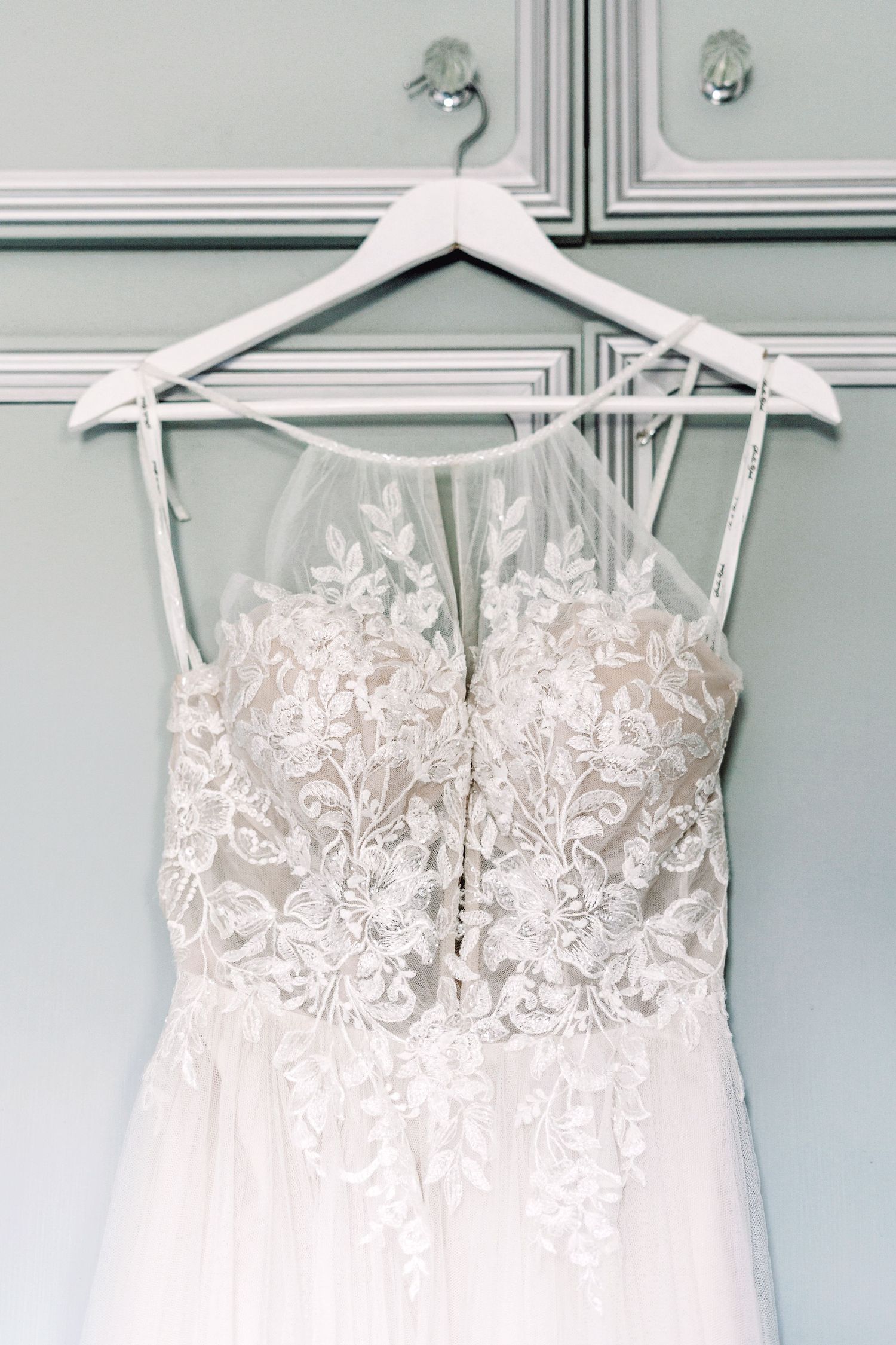 Elegant white wedding dress with lace bodice detail hanging on white wooden hanger.
