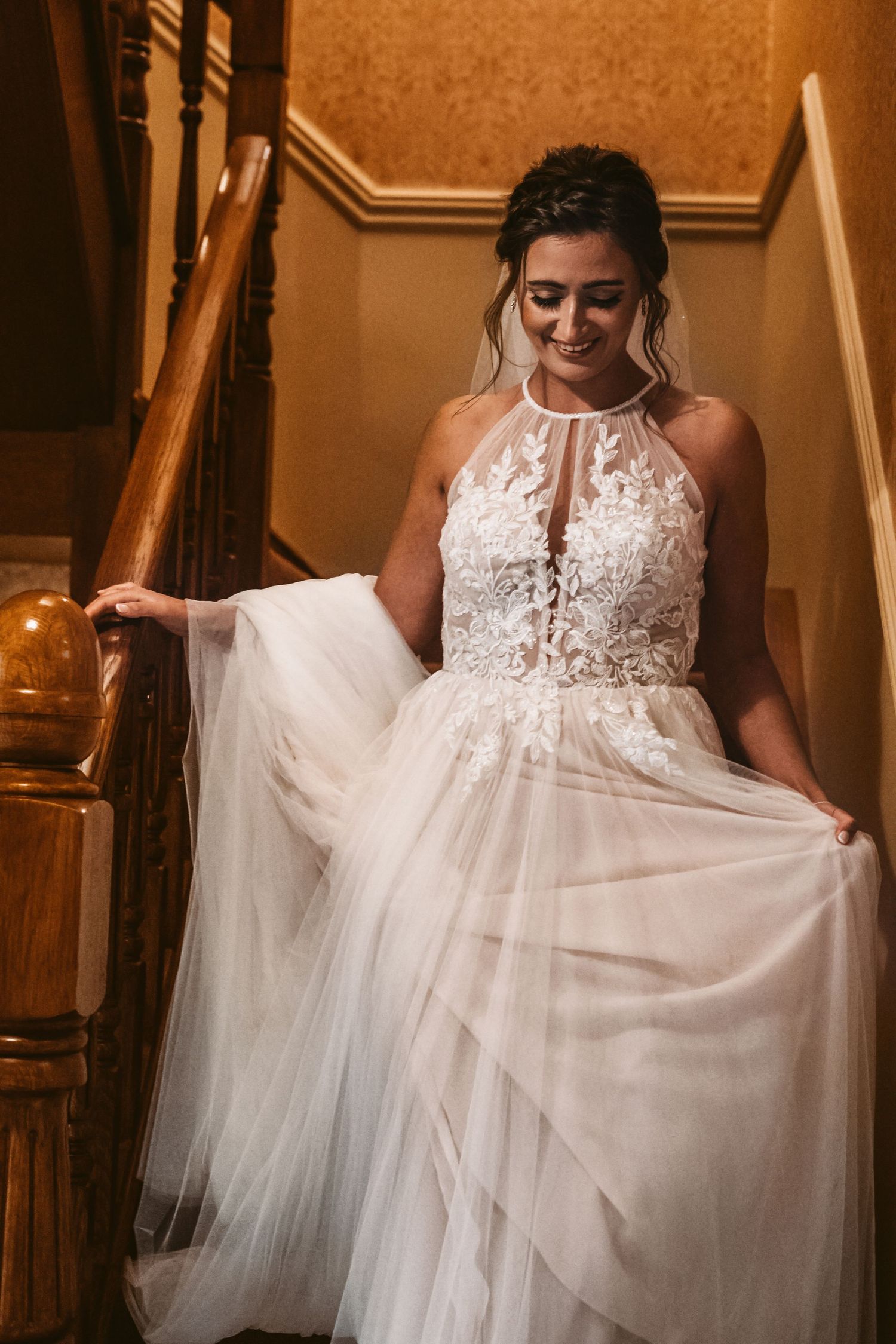 Bride showcases flowing white wedding gown on elegant wooden staircase.