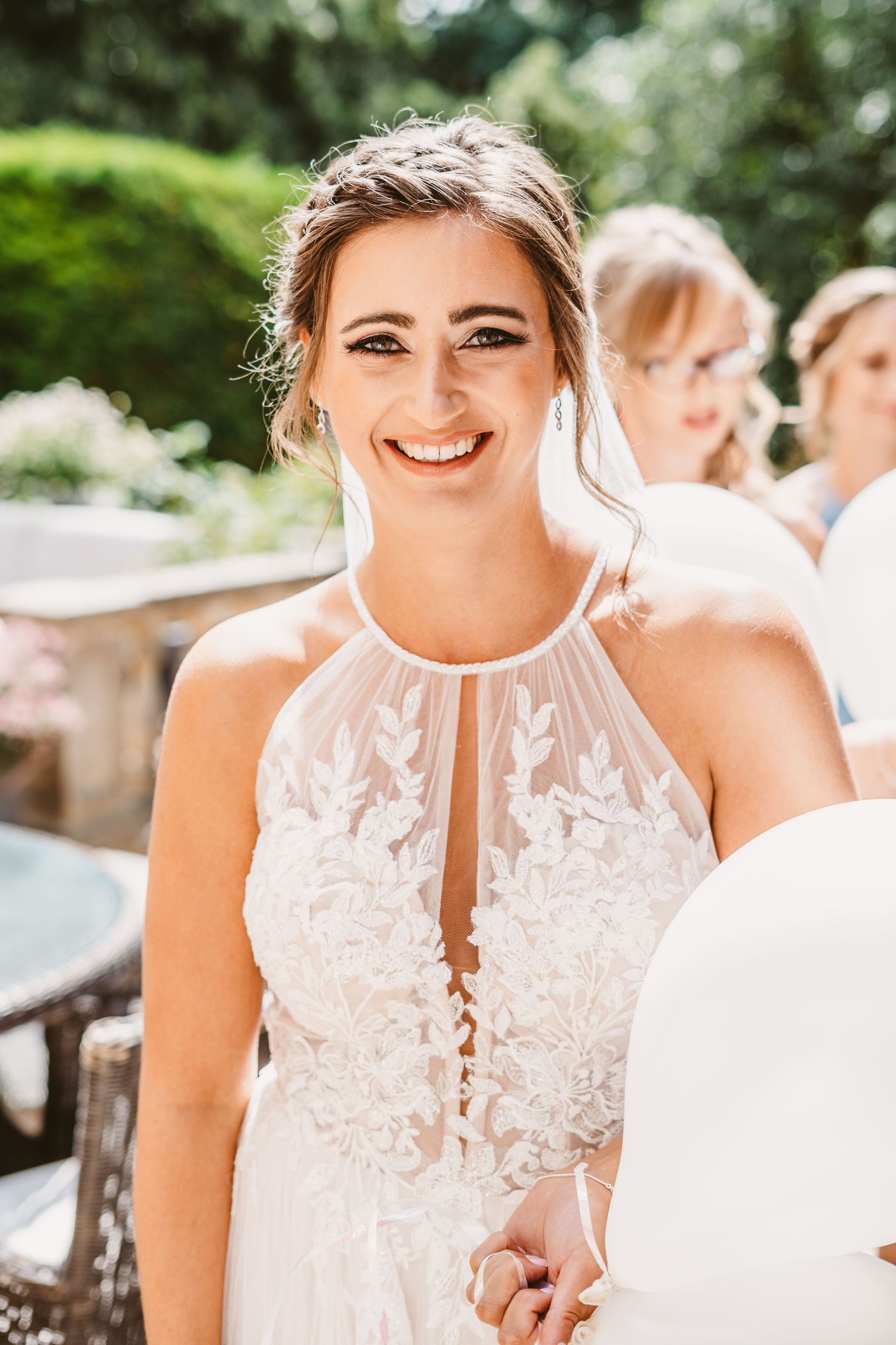 A bride wearing a halter-neck lace gown smiles outdoors on her wedding day.