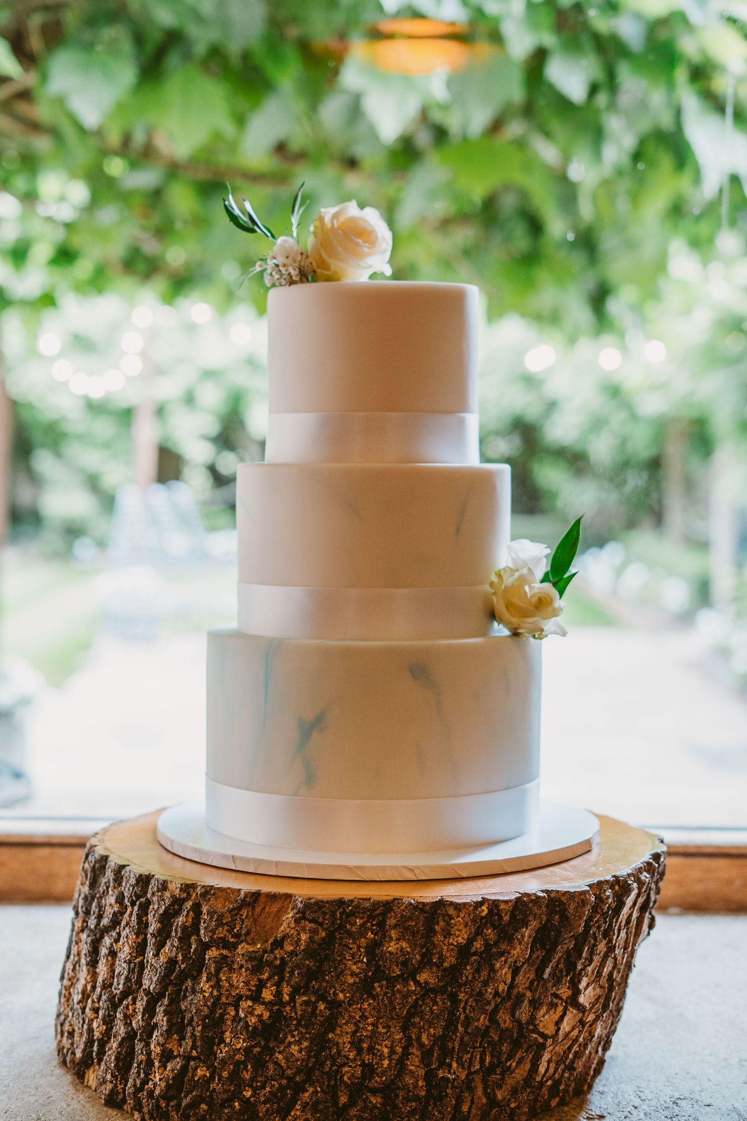 An elegant three-tier white wedding cake adorned with peach roses sits on a rustic wood slice.