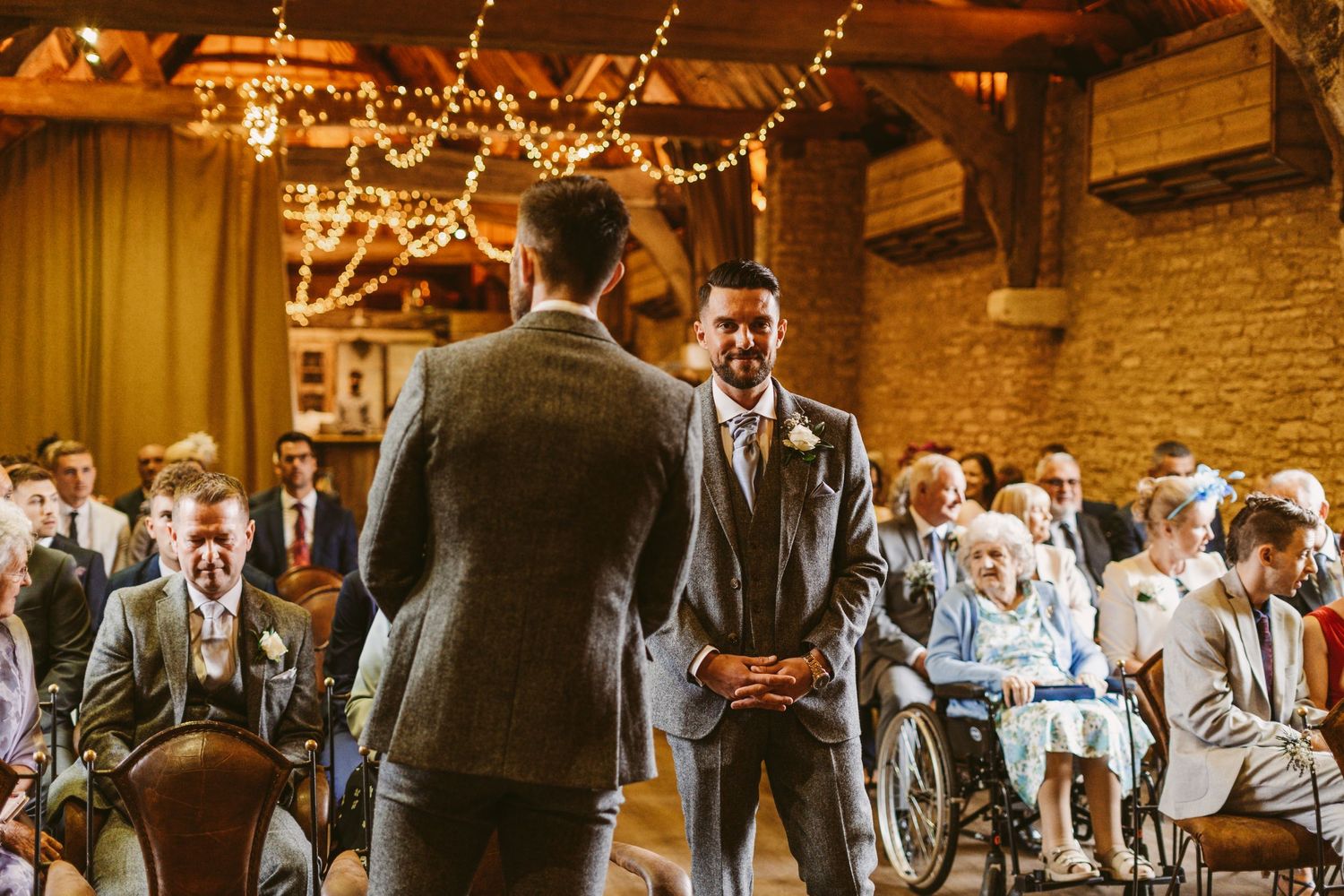 Guests gather under warm string lights in historic brick venue for wedding ceremony.