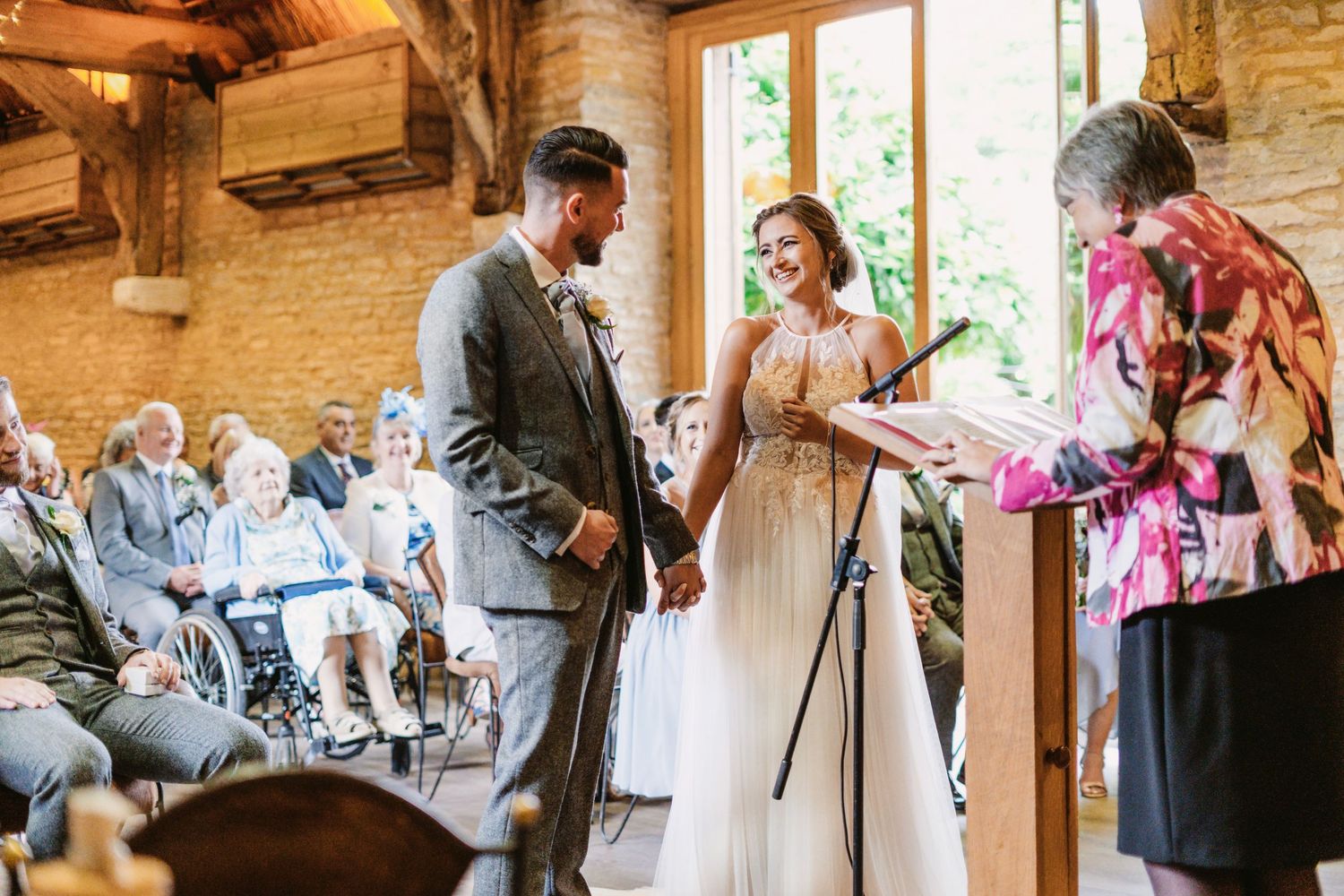 A wedding ceremony unfolds in a charming rustic venue with large windows and wooden details.