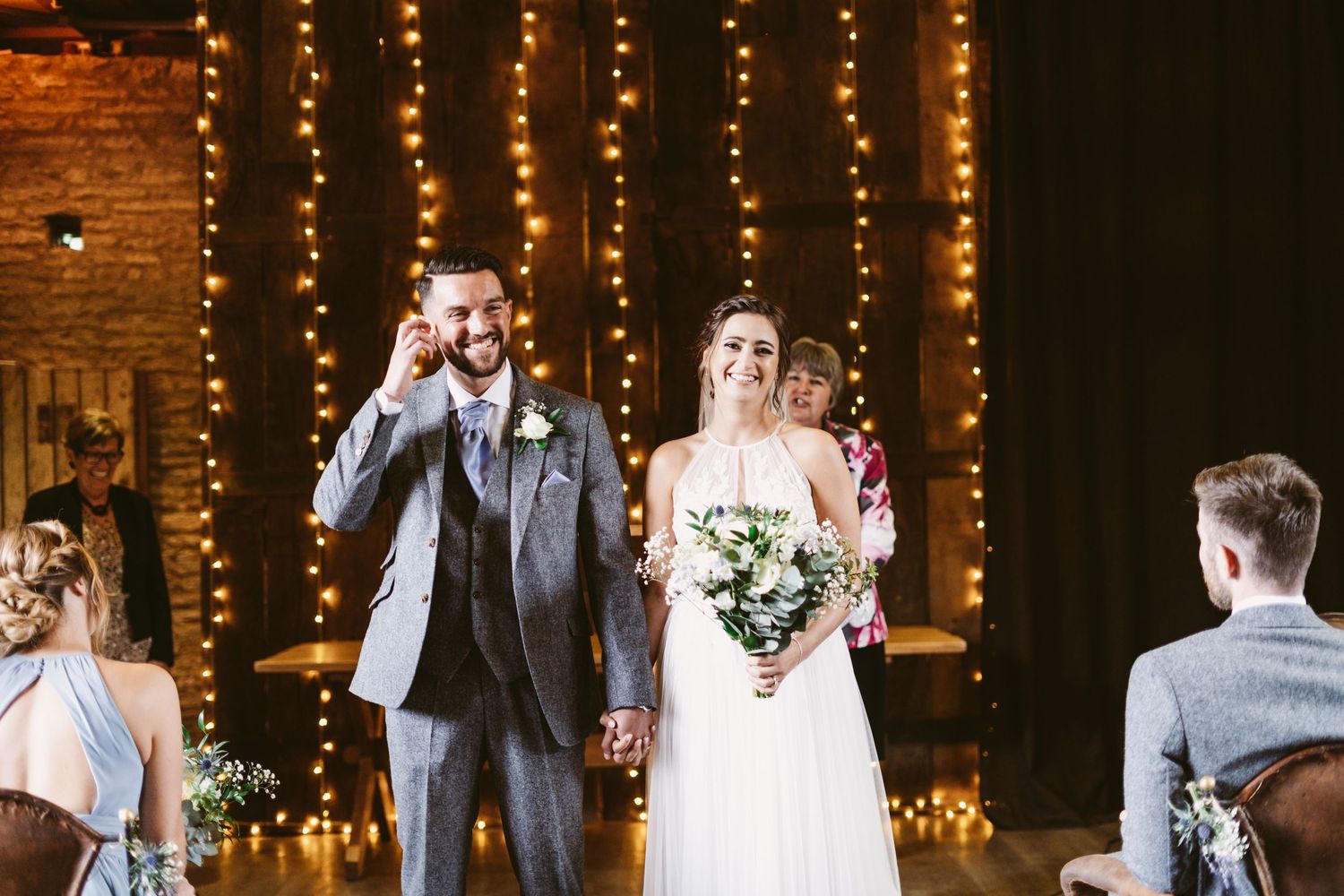 Wedding couple celebrating with string lights and exposed brick backdrop at indoor venue.