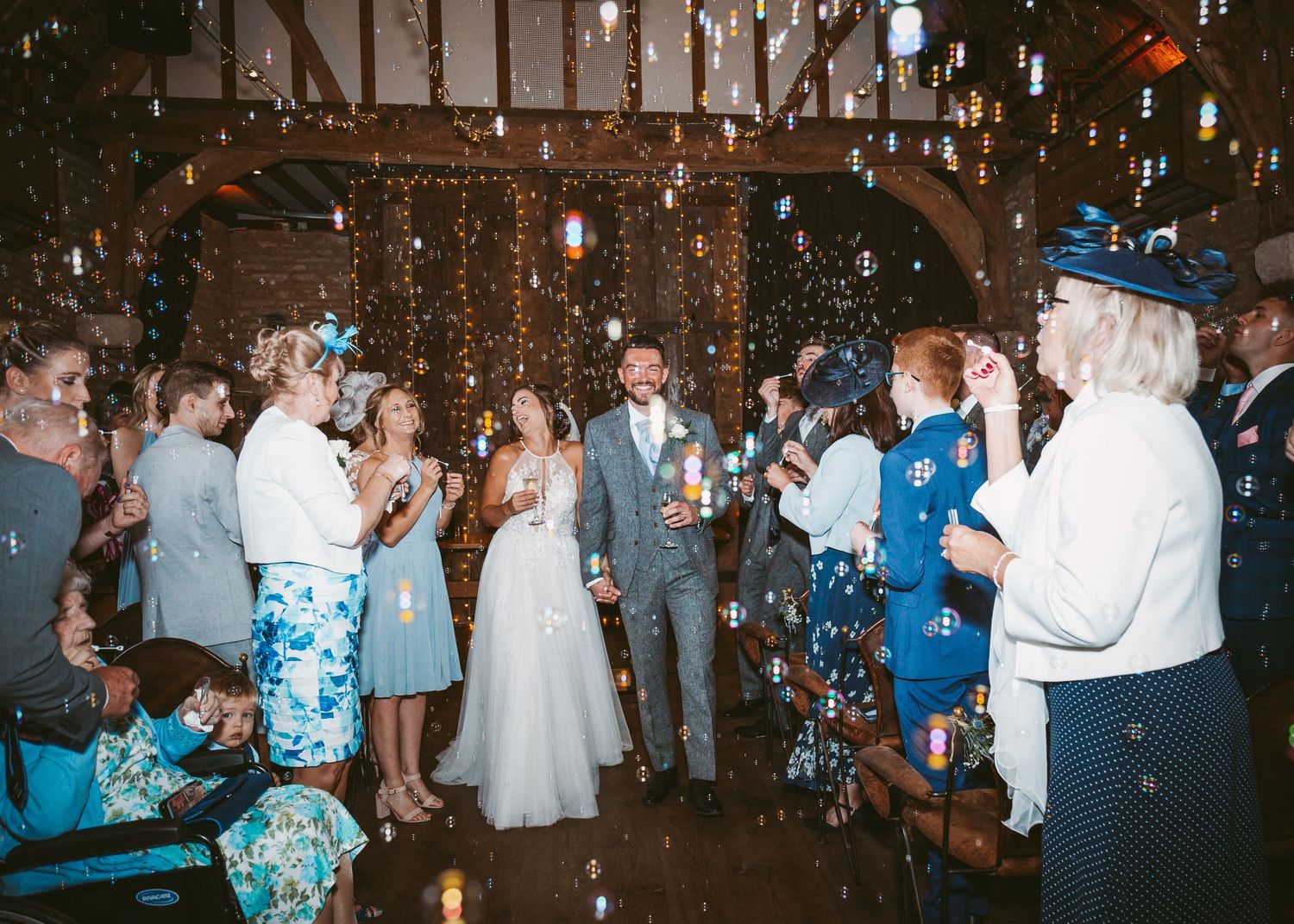 Wedding guests throw confetti at celebration in rustic barn venue with wooden beams.
