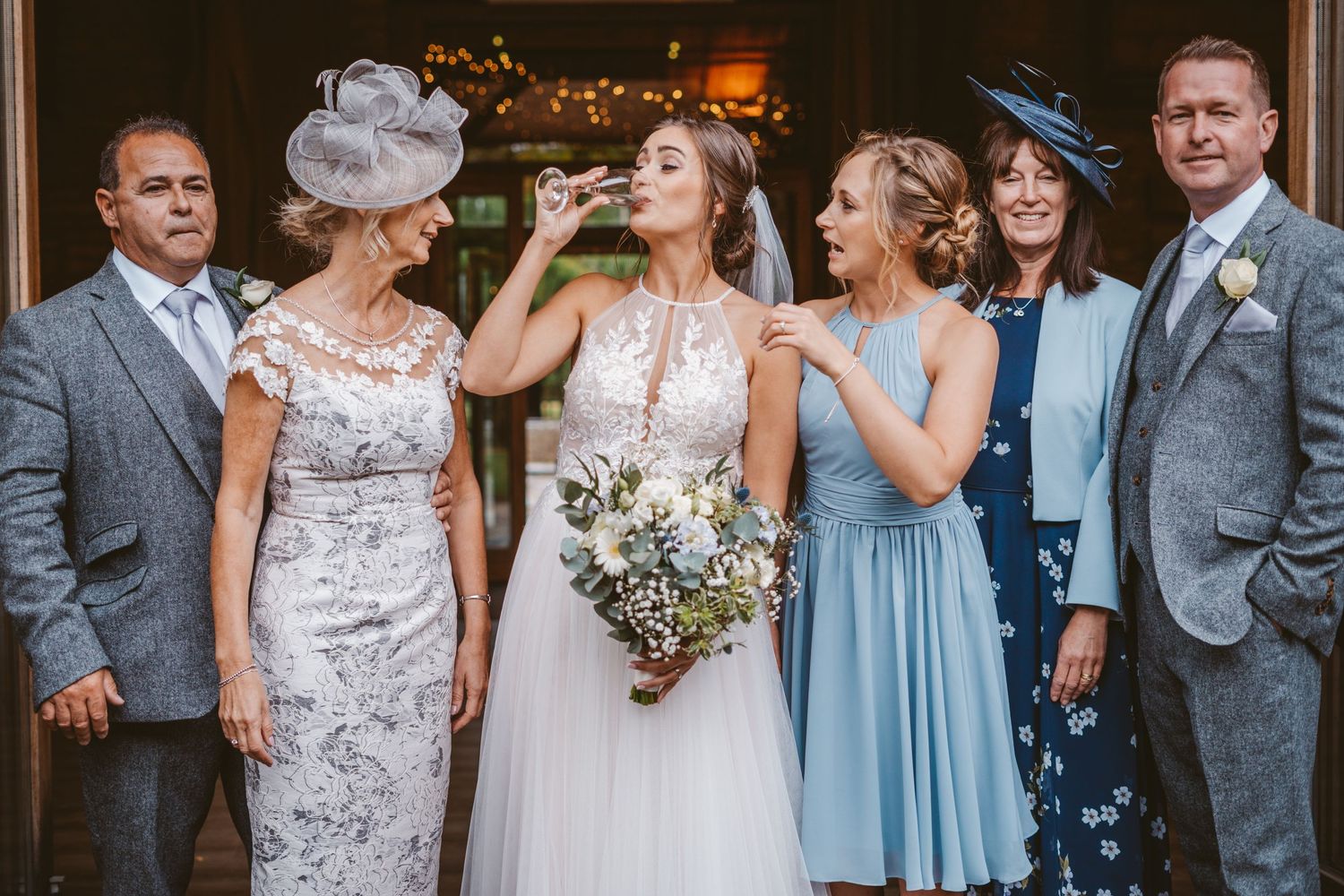 Wedding party sharing champagne while posing in formal attire at venue entrance.