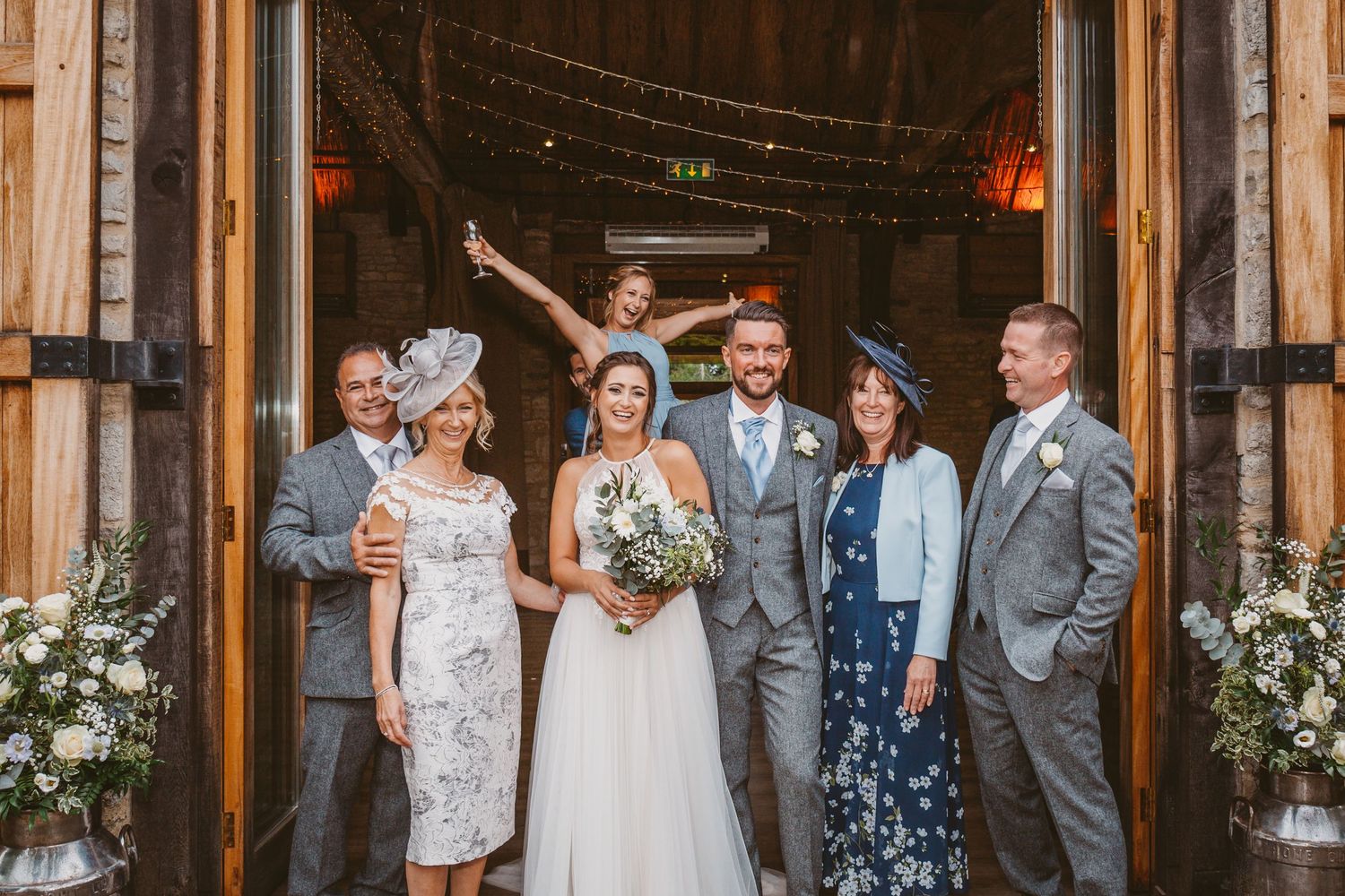 Wedding party poses at the entrance of a rustic barn venue decorated with flowers.