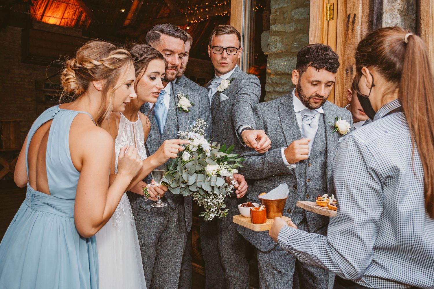 Wedding party gathers for appetizers and drinks in casual conversation outside the venue.