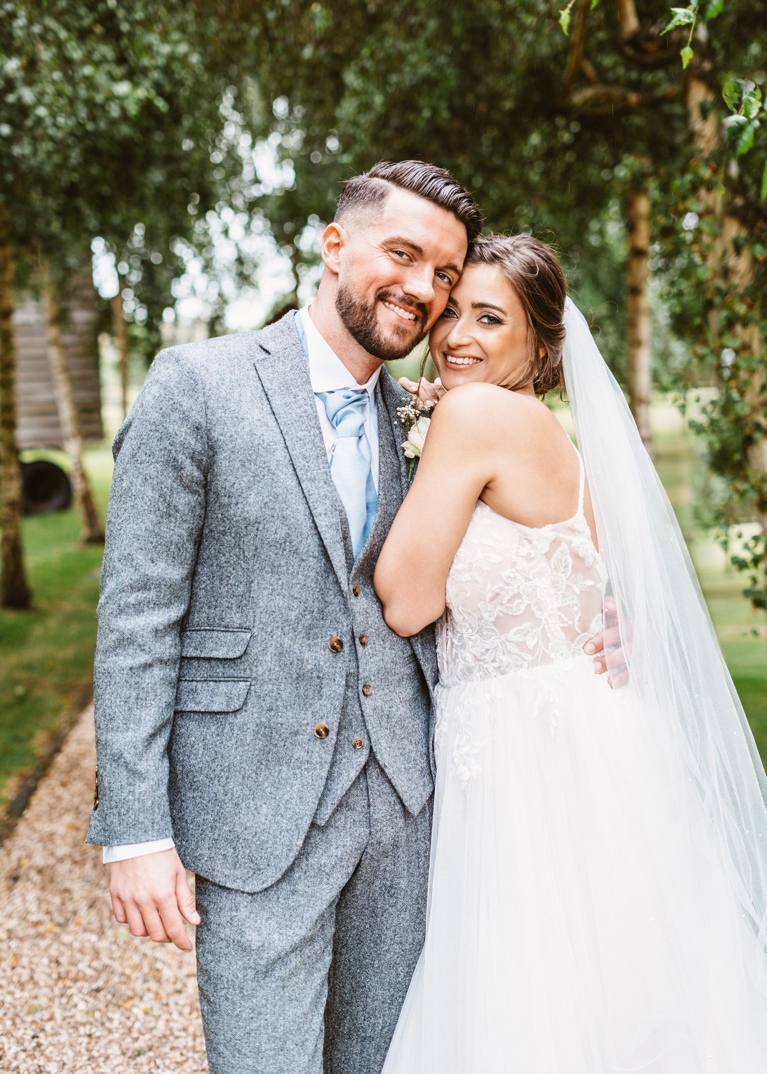 Close-up of newlyweds embracing on garden path surrounded by lush greenery.