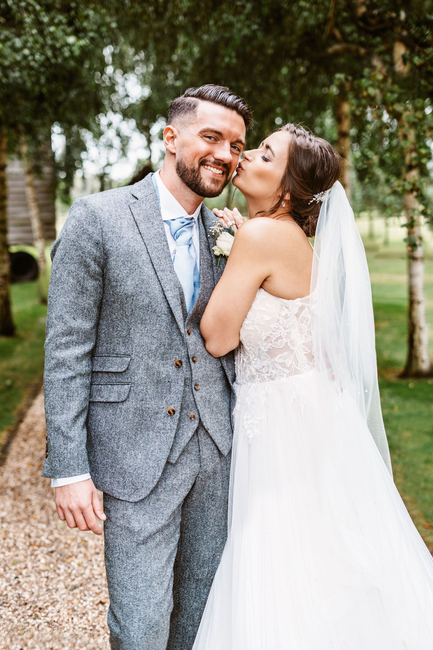 Candid moment of couple in wedding attire sharing a kiss on outdoor path.