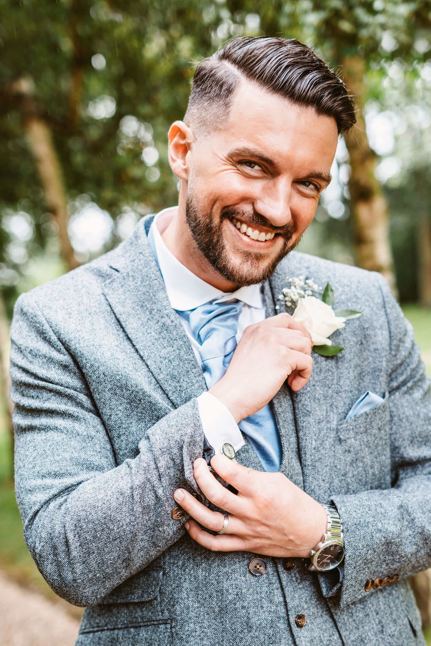 Close-up portrait of groom adjusting suit jacket while wearing light blue tie.