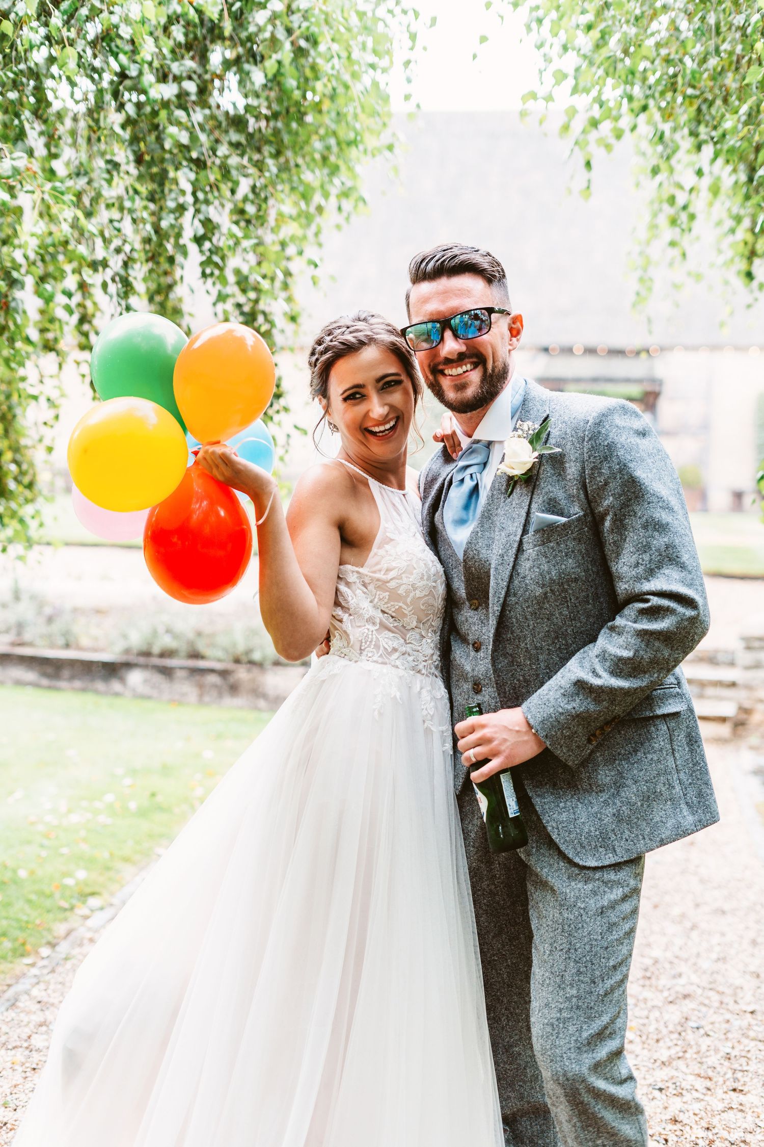 Newlyweds share cheerful laughter while holding bright balloons against a natural backdrop.