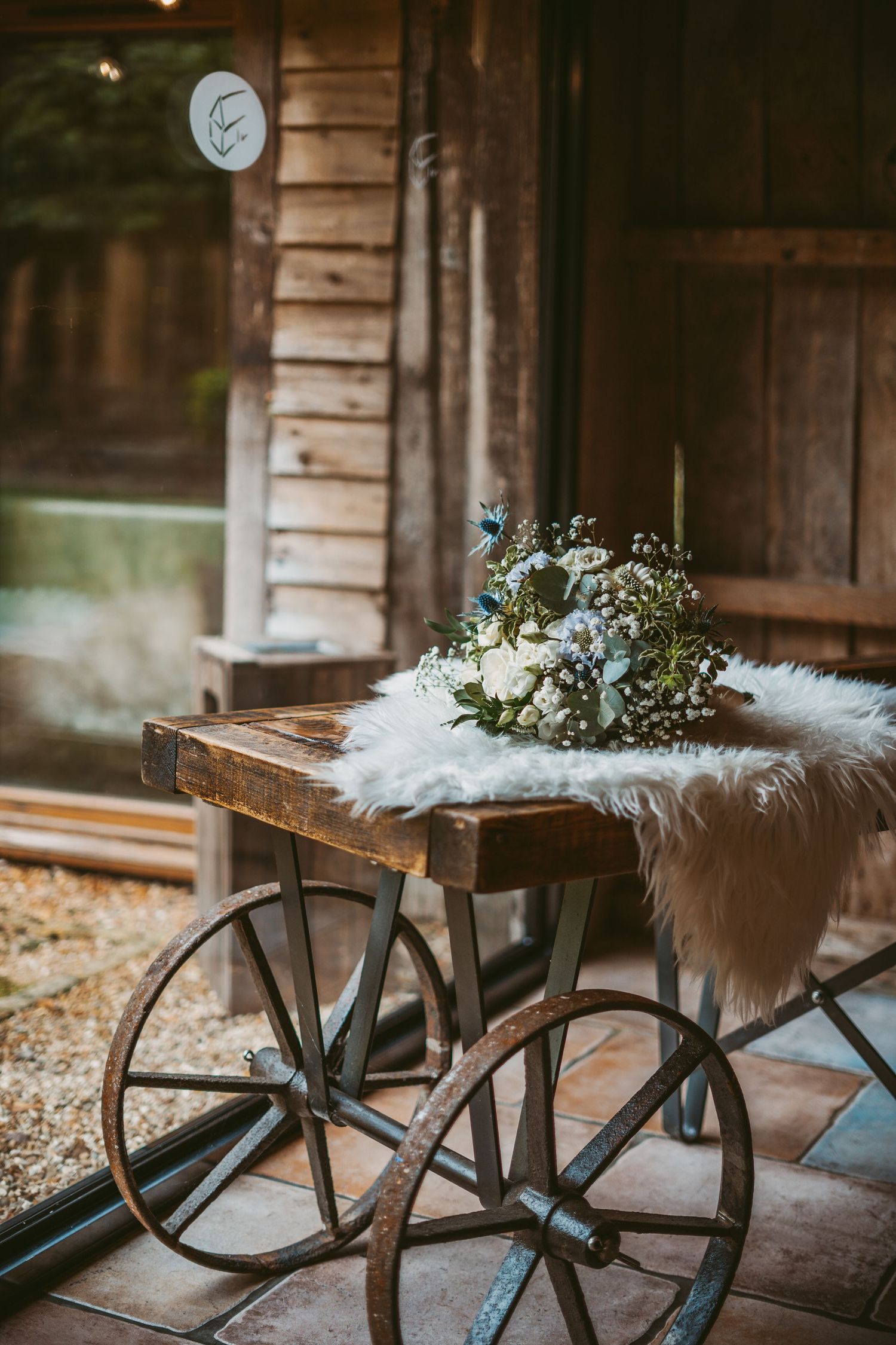 Wedding bouquet with white flowers displayed on rustic wooden cart with fur overlay.